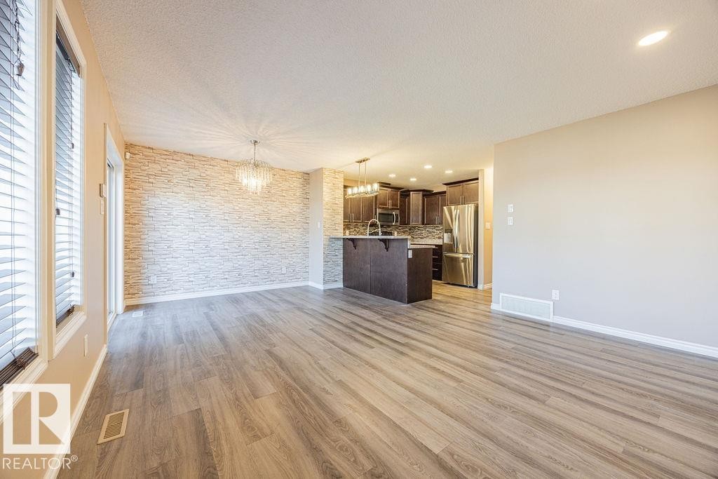 Open-concept living space featuring wood-finish flooring, a decorative stone accent wall, and a crystal chandelier - 14 9350 211 Street, Edmonton, AB - Indoor