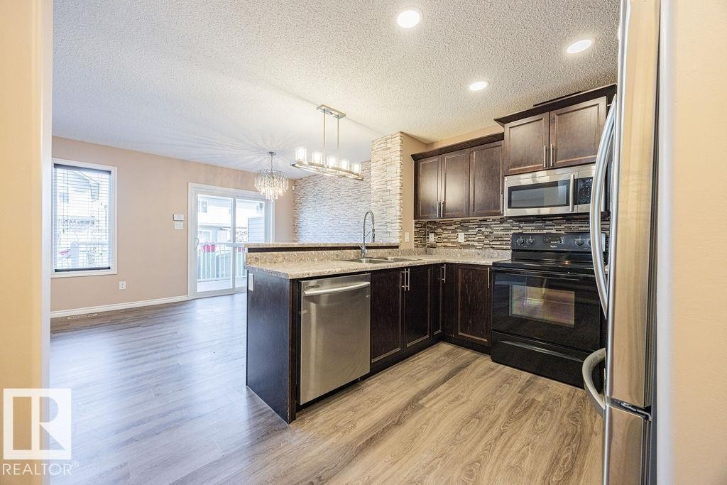 Kitchen featuring dark wood cabinetry, stainless steel appliances, and a stone-look countertop - 14 9350 211 Street, Edmonton, AB - Indoor Photo Showing Kitchen With Upgraded Kitchen