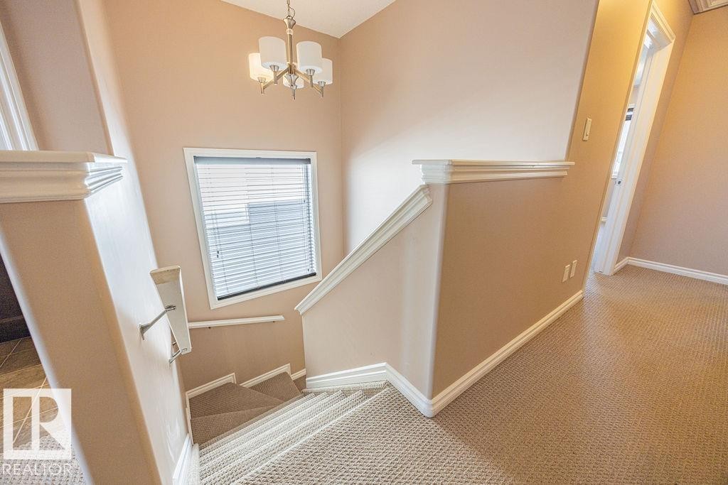 Carpeted staircase with white trim, a landing window featuring blinds, and a brass-tone chandelier - 14 9350 211 Street, Edmonton, AB - Indoor Photo Showing Other Room