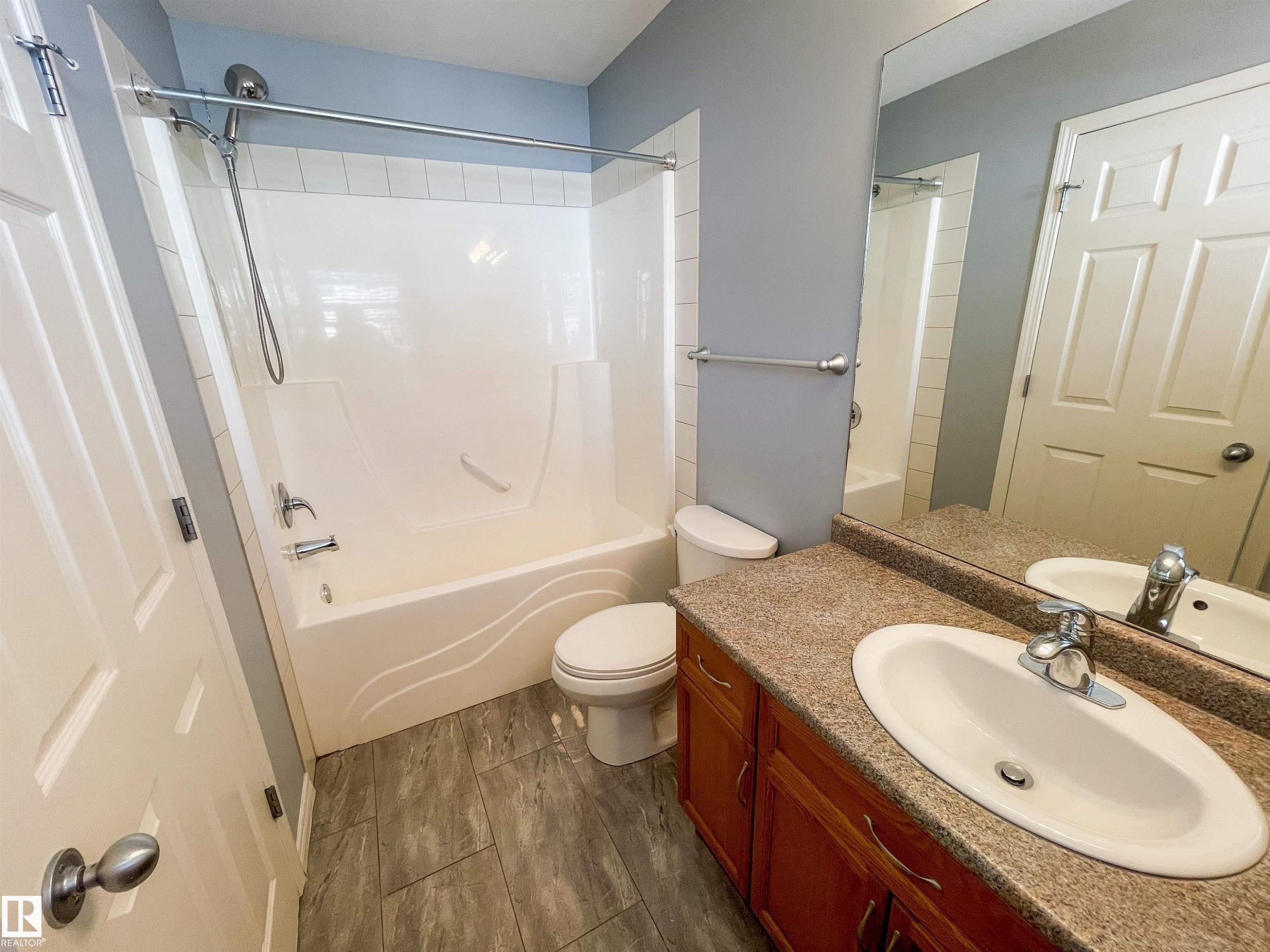 Bathroom with tile-finish flooring, a combination tub and shower with a white surround, and a vanity featuring a speckled countertop, integrated sink, and wood cabinetry - 5806 118 Avenue Nw, Edmonton, AB - Indoor Photo Showing Bathroom