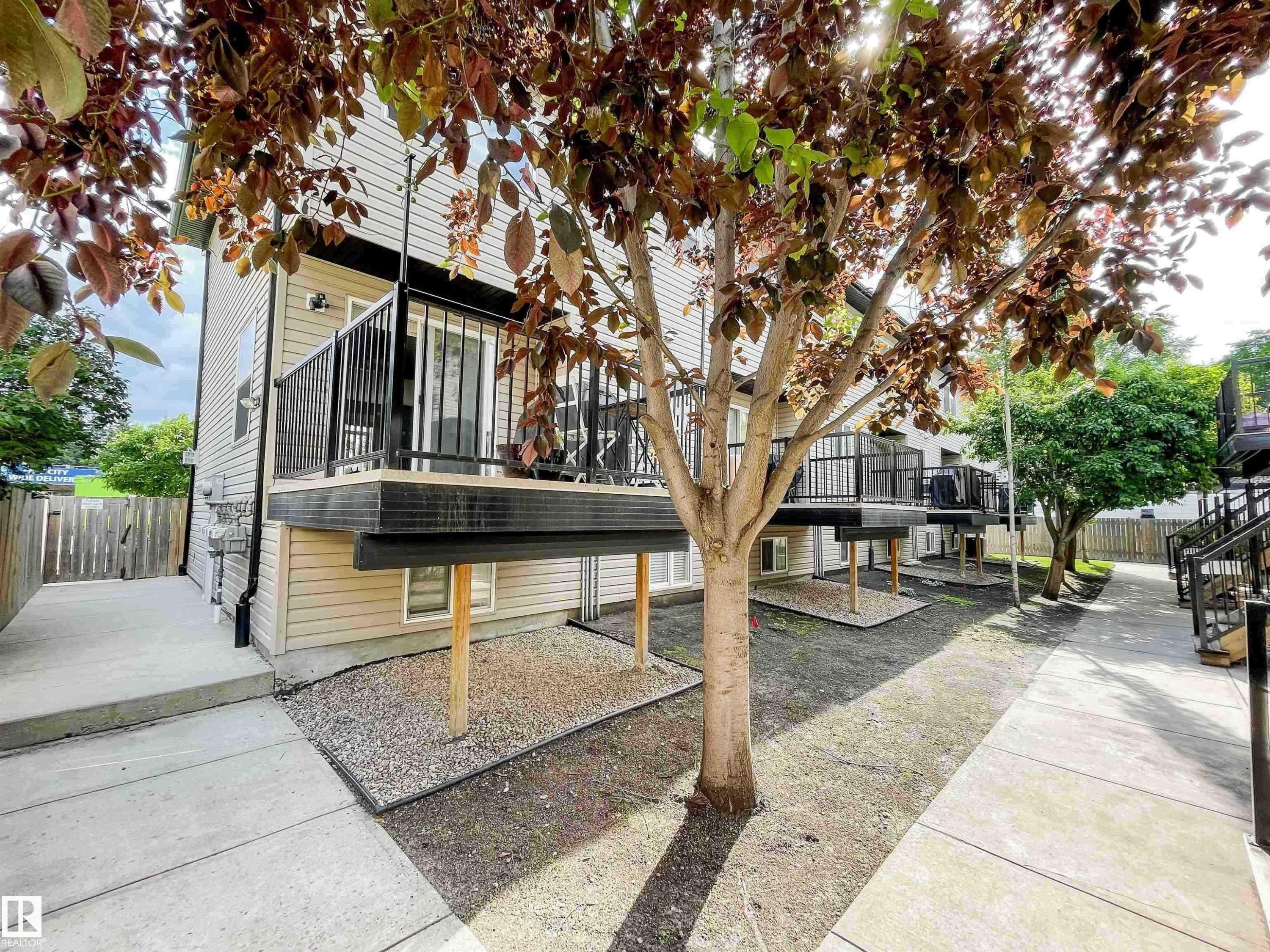 Exterior featuring light-colored siding, multiple elevated decks with black railings, and mature trees providing natural screening - 5806 118 Avenue Nw, Edmonton, AB - Outdoor