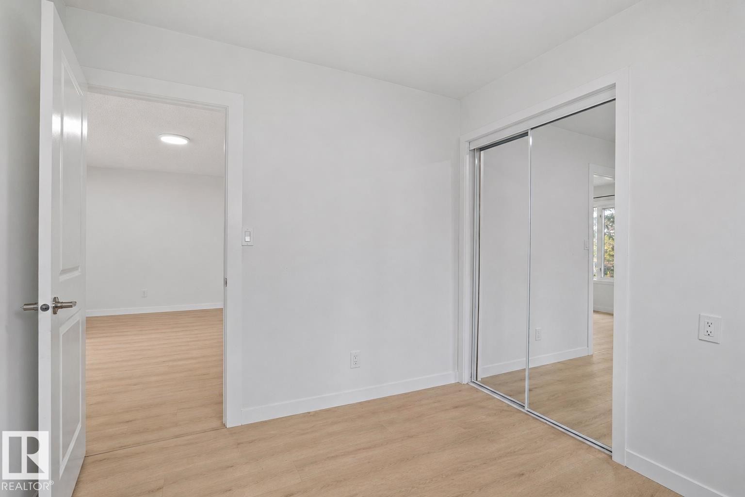 Bright interior space featuring light wood-finish flooring, white walls, and a mirrored closet - 1566 Lakewood Road Nw, Edmonton, AB - Indoor Photo Showing Other Room