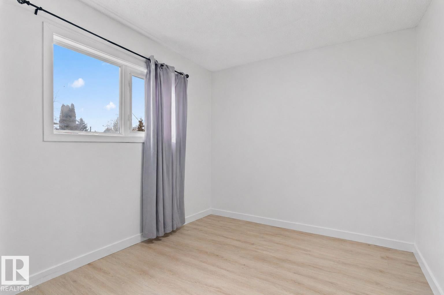 Bright interior space featuring a window with white trim, light wood-finish flooring, and crisp white walls - 1566 Lakewood Road Nw, Edmonton, AB - Indoor Photo Showing Other Room
