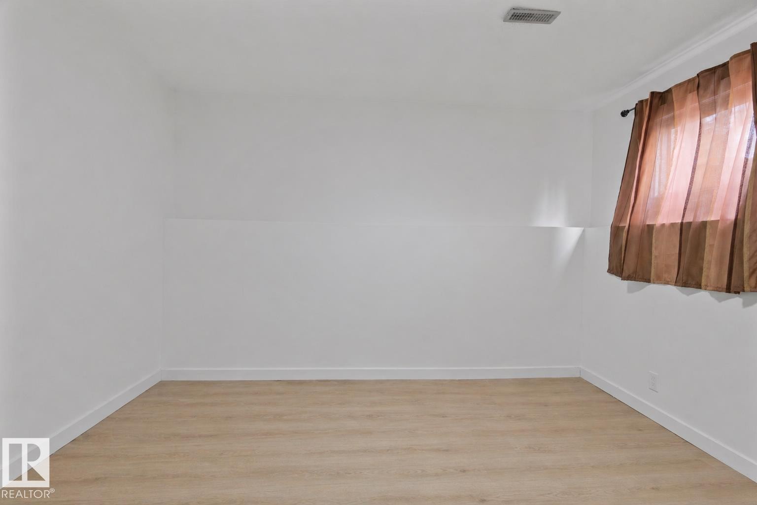 Spacious room featuring light wood-finish flooring, white walls, and a window with brown sheer drapes - 1566 Lakewood Road Nw, Edmonton, AB - Indoor Photo Showing Other Room