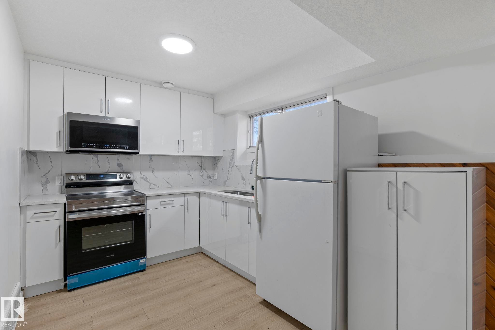 Contemporary kitchen featuring white cabinetry, light countertops, and a white backsplash - 1566 Lakewood Road Nw, Edmonton, AB - Indoor Photo Showing Kitchen