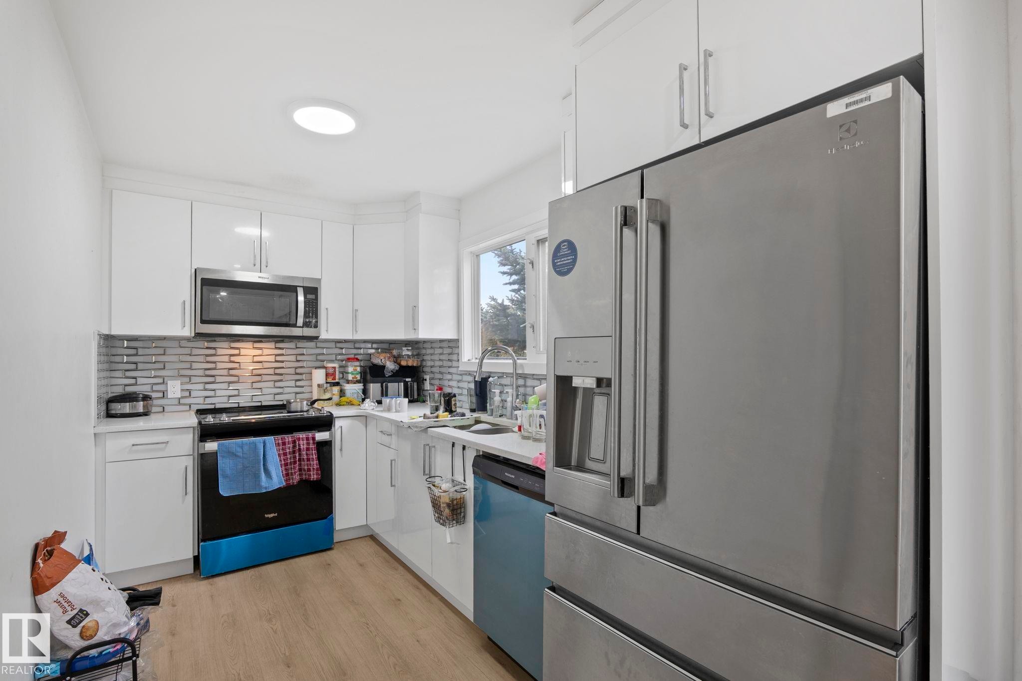 Kitchen featuring white cabinetry, a subway tile backsplash, stainless steel appliances, wood-finish flooring, and a circular ceiling light fixture - 1566 Lakewood Road Nw, Edmonton, AB - Indoor Photo Showing Kitchen With Upgraded Kitchen
