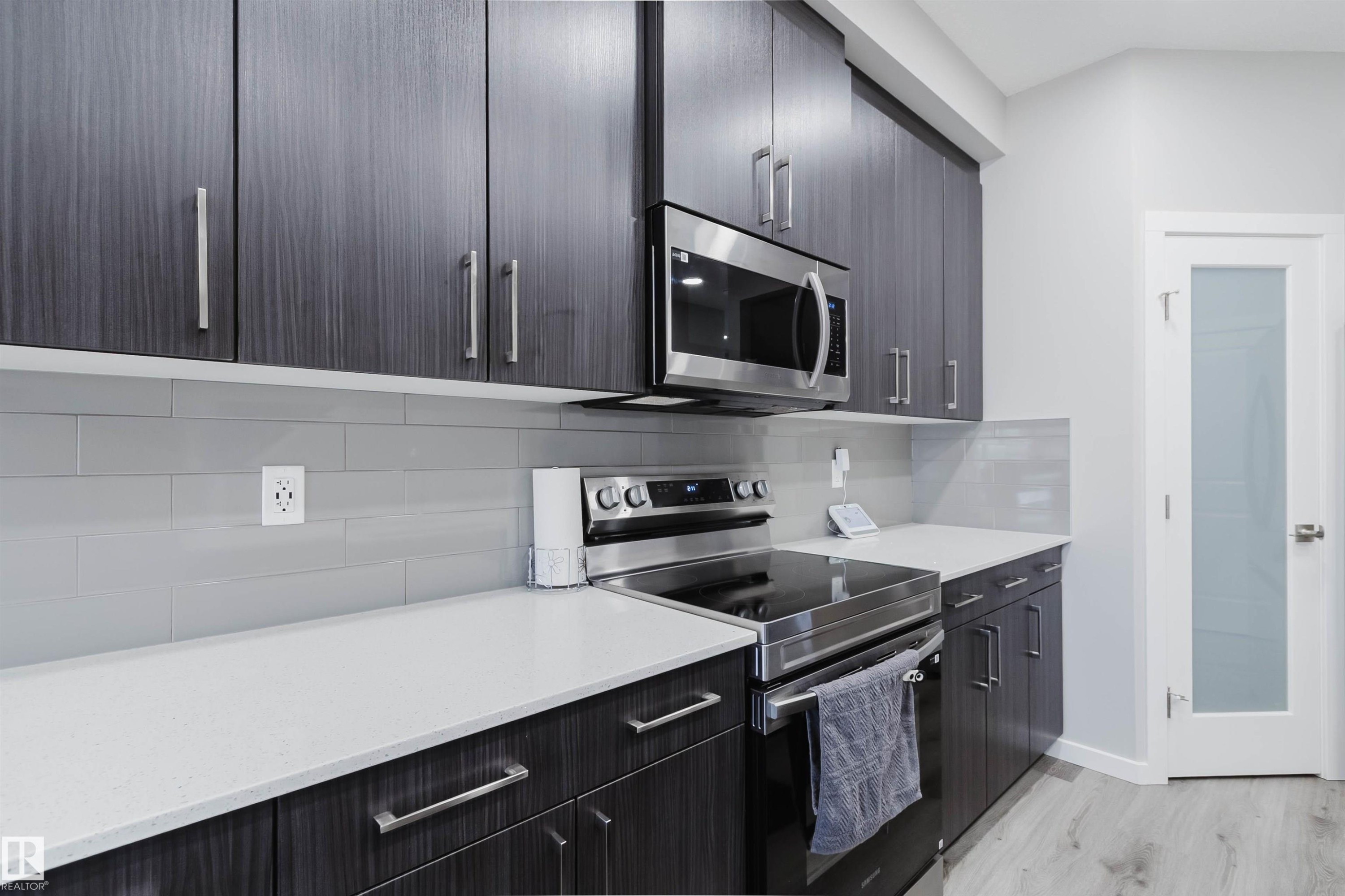 Modern kitchen featuring dark wood-finish cabinetry with stainless steel hardware, light-toned countertops, and a subway tile backsplash - 343 Edgemont Drive, Edmonton, AB - Indoor Photo Showing Kitchen