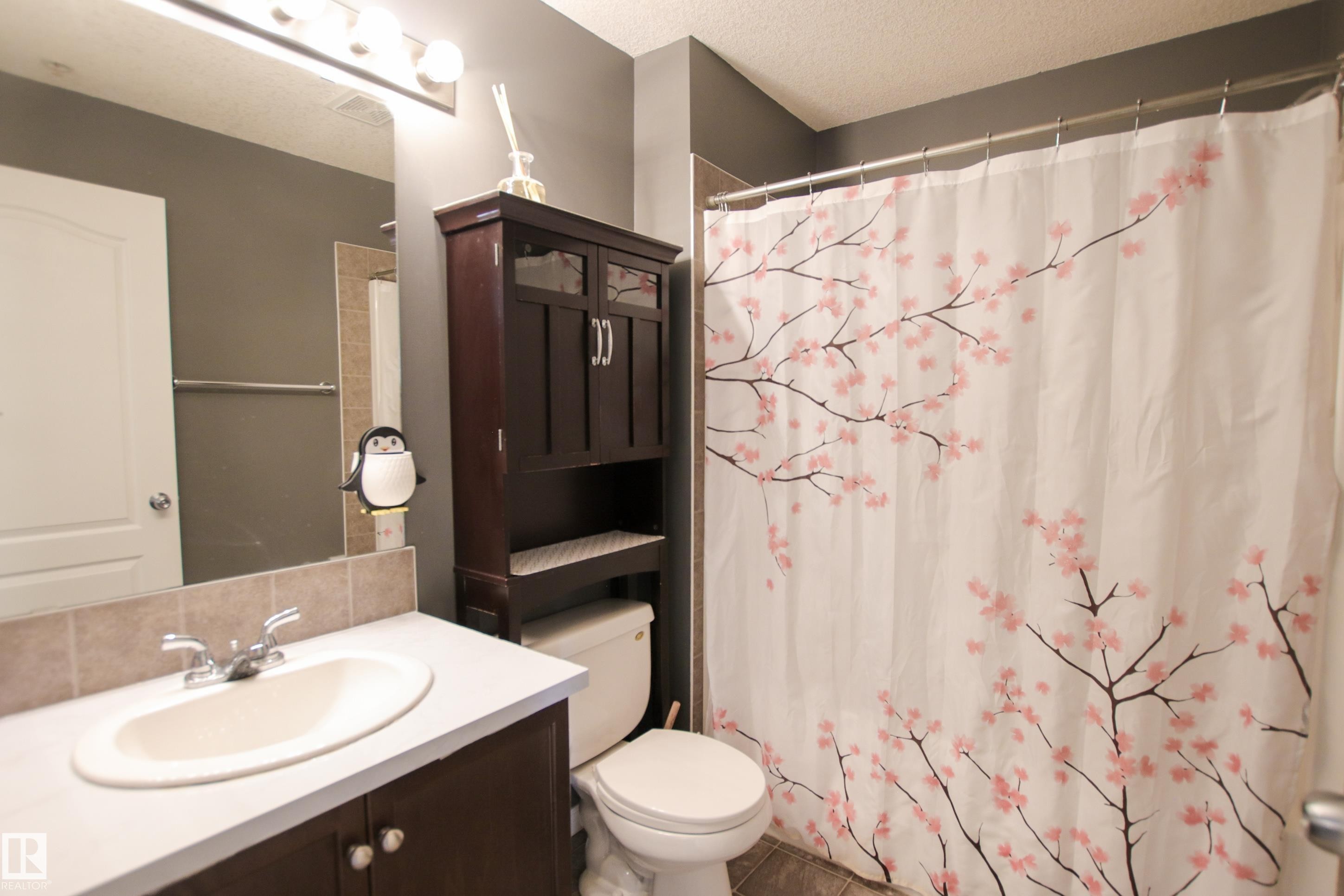 Bathroom featuring a vanity with an integrated sink, a large wall-mounted mirror, a built-in over-the-toilet storage cabinet, a toilet, and a shower with a chrome rod - 7206 7327 South Terwillegar Drive, Edmonton, AB - Indoor Photo Showing Bathroom