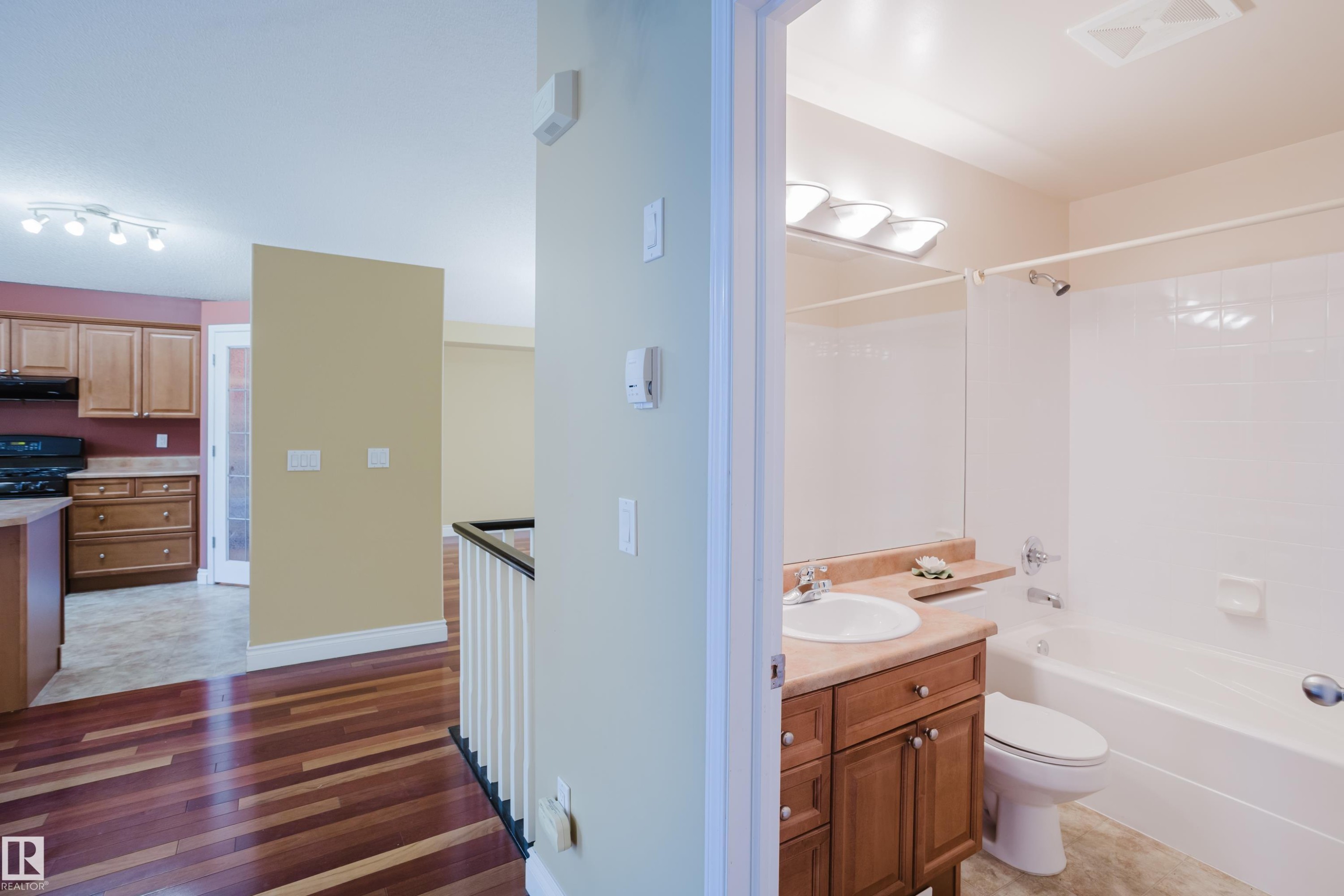 Bathroom featuring a vanity with wood-finish cabinetry, a built-in sink, and a mirrored wall - 9 102 Bridgeport Crossing, Leduc, AB - Indoor Photo Showing Bathroom