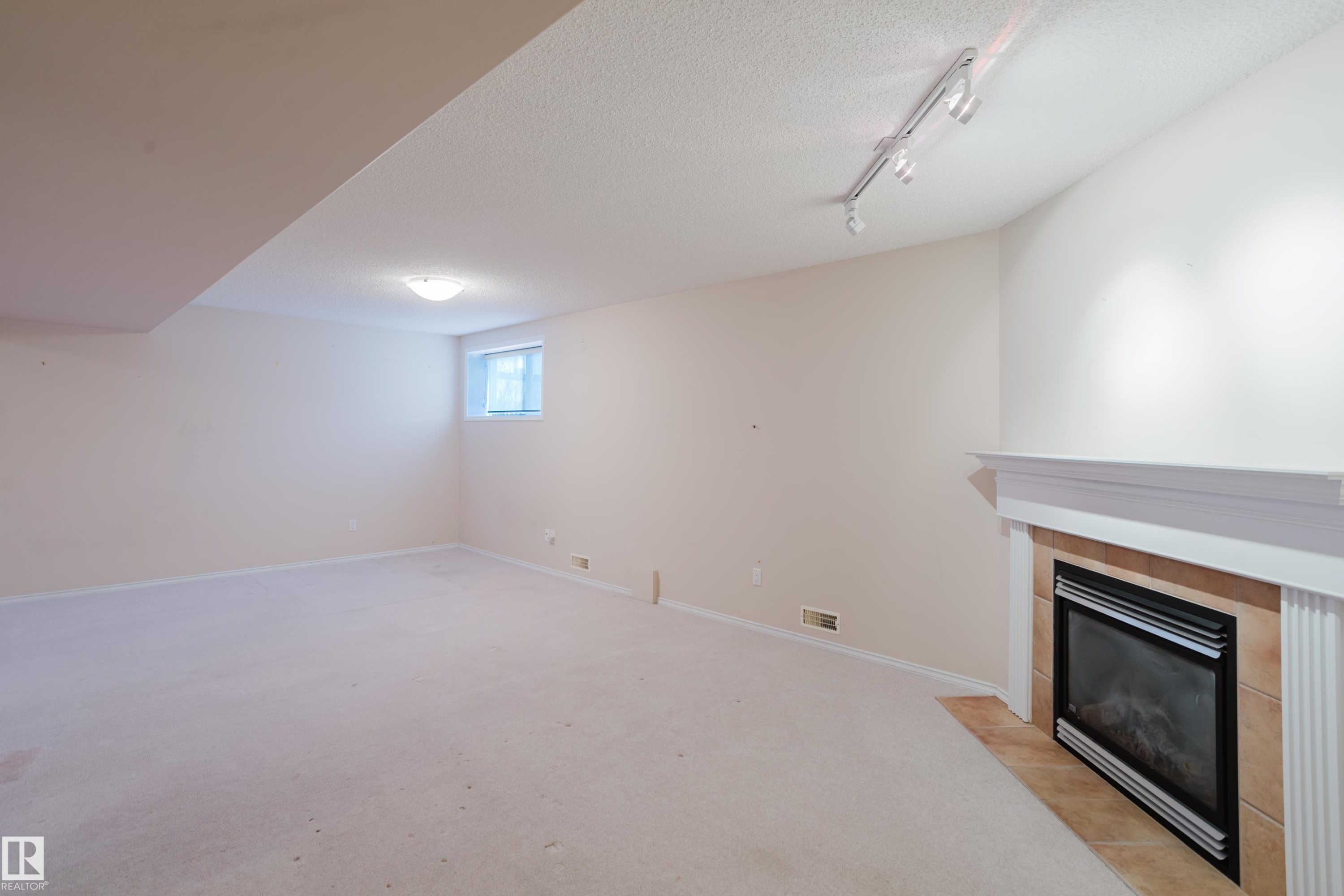 Expansive room featuring a built-in fireplace with a white mantelpiece and tile surround - 9 102 Bridgeport Crossing, Leduc, AB - Indoor With Fireplace