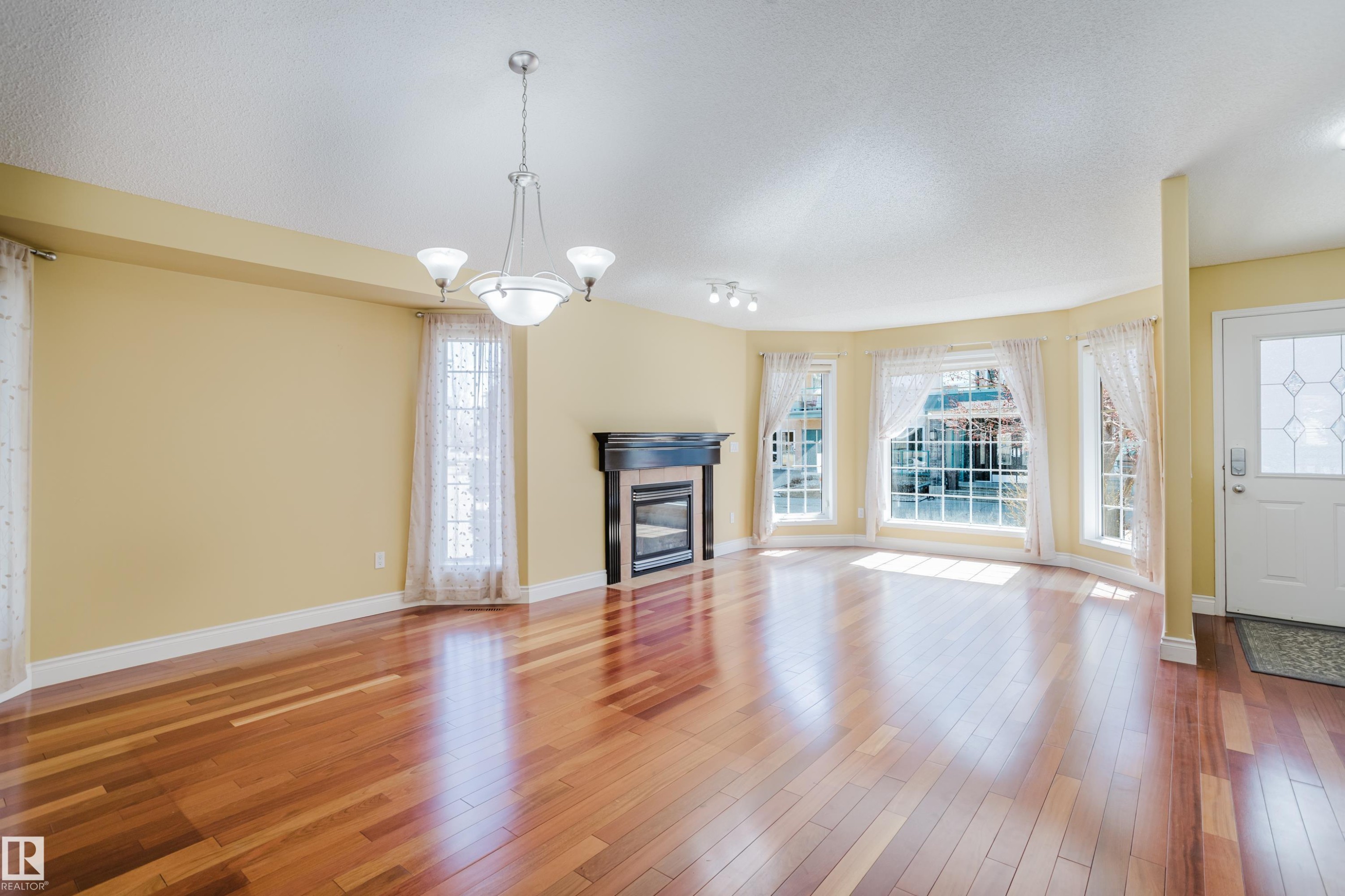 Spacious interior featuring wood-finish flooring, a decorative fireplace with a dark mantel, and multiple windows with white trim - 9 102 Bridgeport Crossing, Leduc, AB - Indoor Photo Showing Living Room With Fireplace