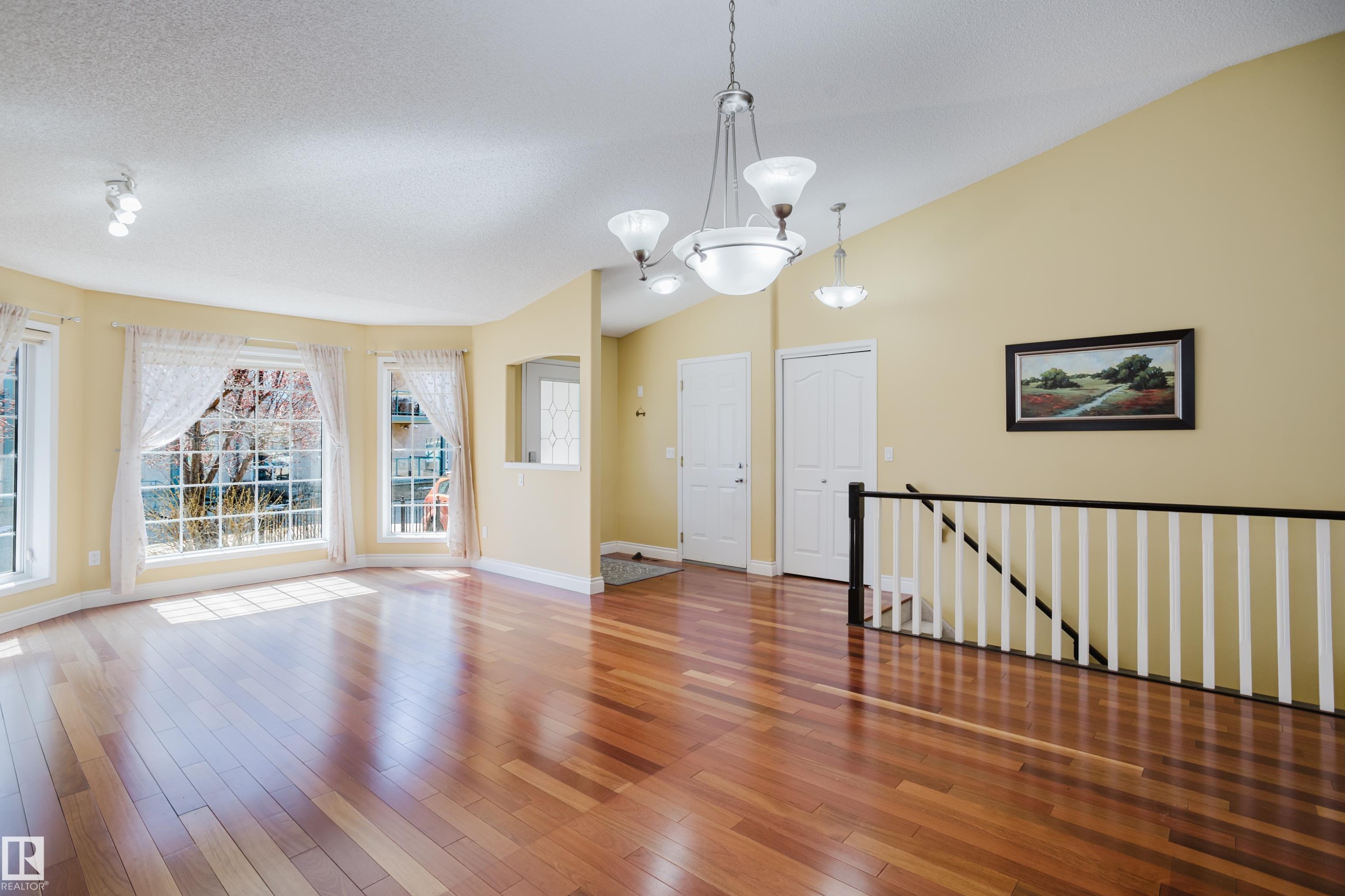 Expansive room featuring wood-finish flooring, a vaulted ceiling, and multiple windows - 9 102 Bridgeport Crossing, Leduc, AB - Indoor