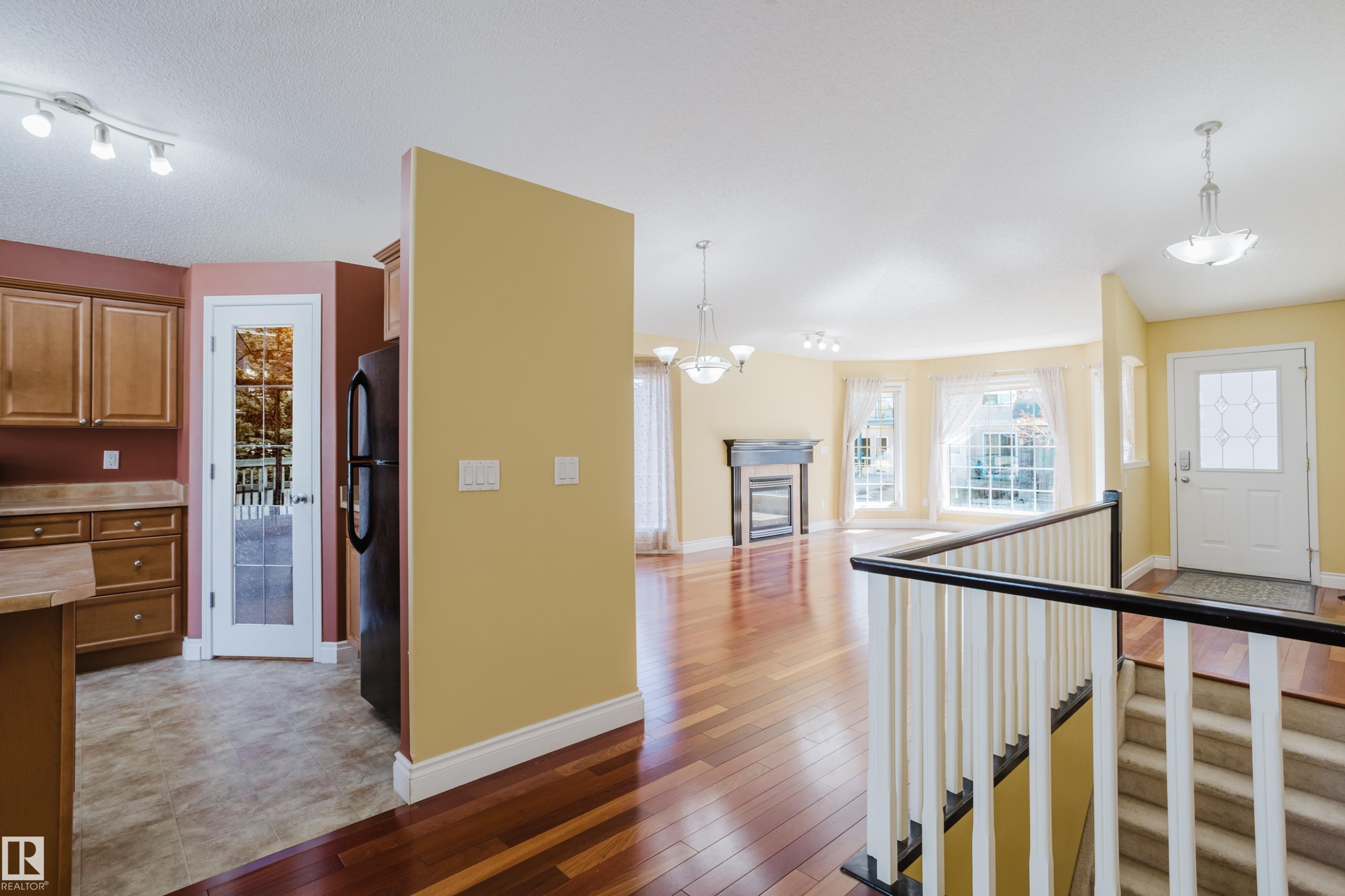 Open-concept living space with wood-finish flooring, a detailed fireplace, and a bay window - 9 102 Bridgeport Crossing, Leduc, AB - Indoor Photo Showing Other Room