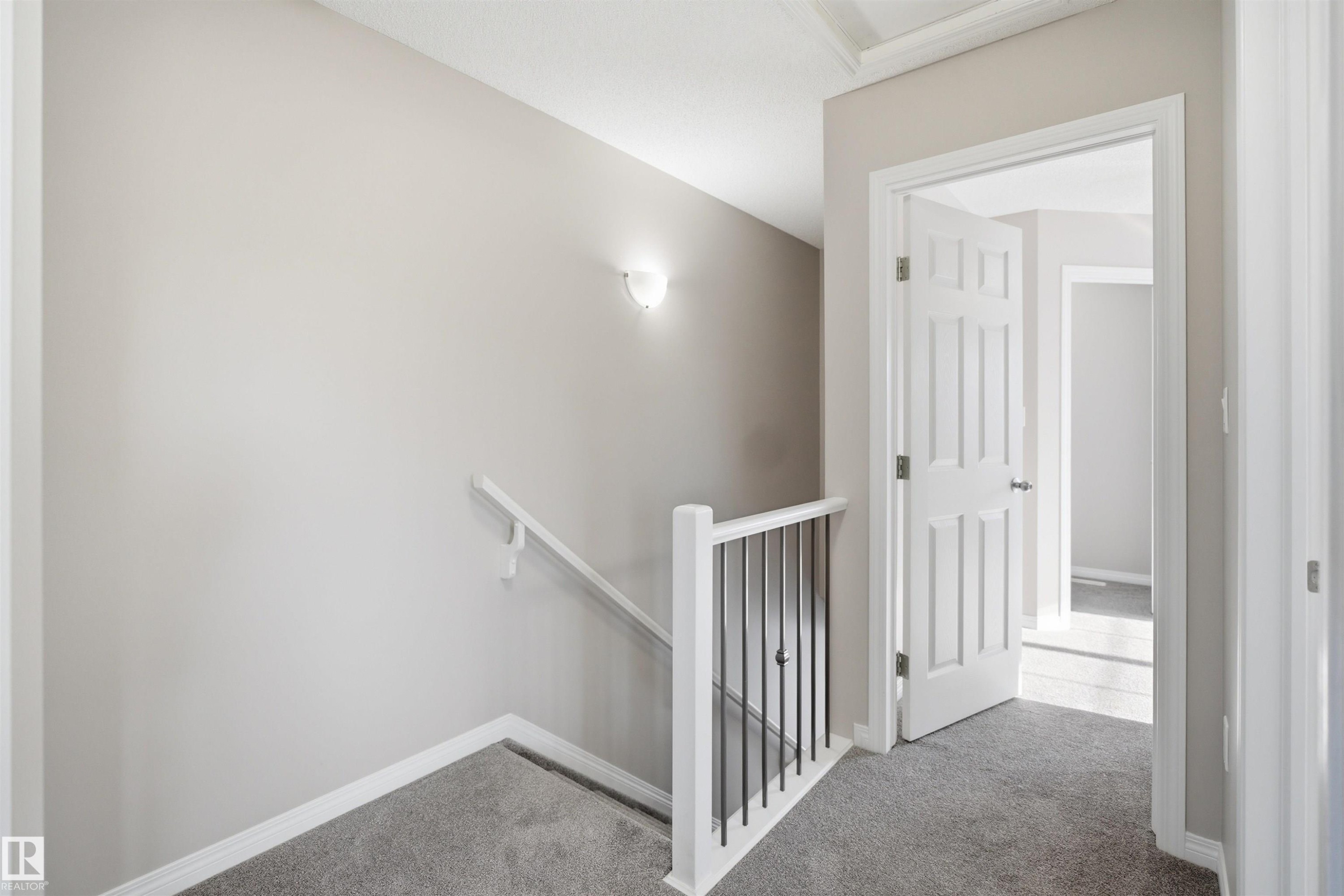 Upper-level landing featuring neutral-toned walls, gray carpeting, a white panel door, and a white handrail with black metal balusters - 33 7385 Edgemont Way Nw, Edmonton, AB - Indoor Photo Showing Other Room