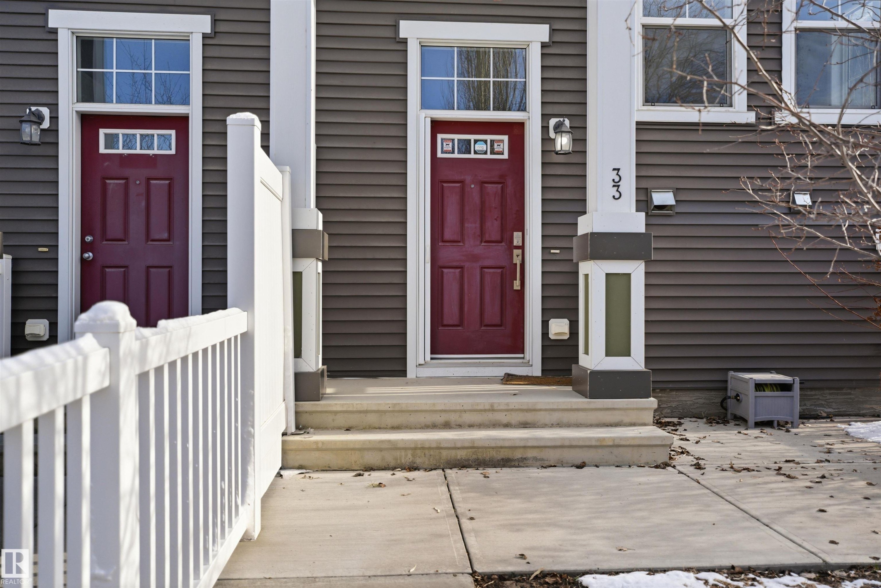 Modern townhouse exterior featuring gray horizontal siding and a striking red paneled entry door - 33 7385 Edgemont Way Nw, Edmonton, AB - Outdoor