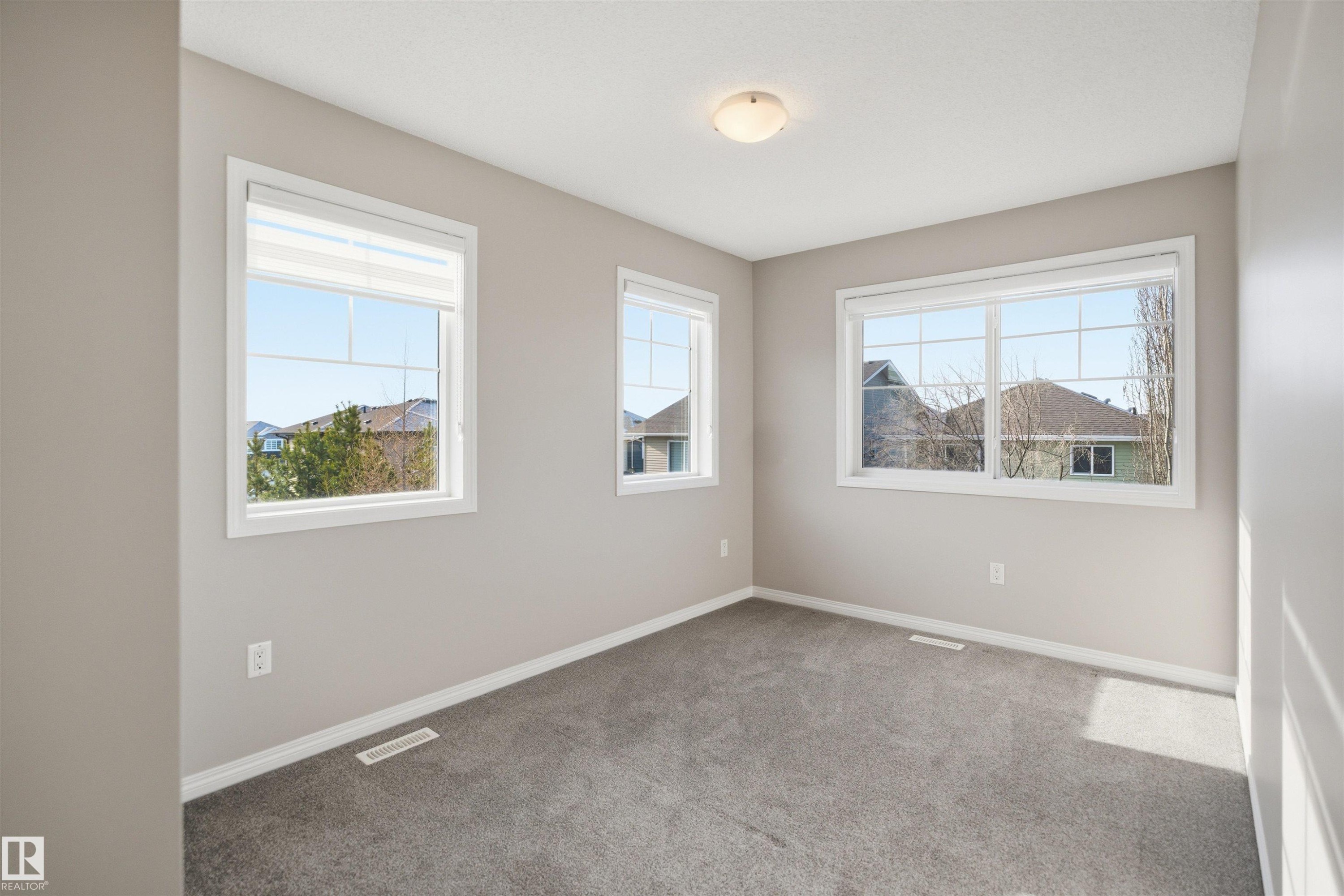 Bright room featuring three large windows with white trim, gray plush carpeting, and light neutral wall paint - 33 7385 Edgemont Way Nw, Edmonton, AB - Indoor Photo Showing Other Room