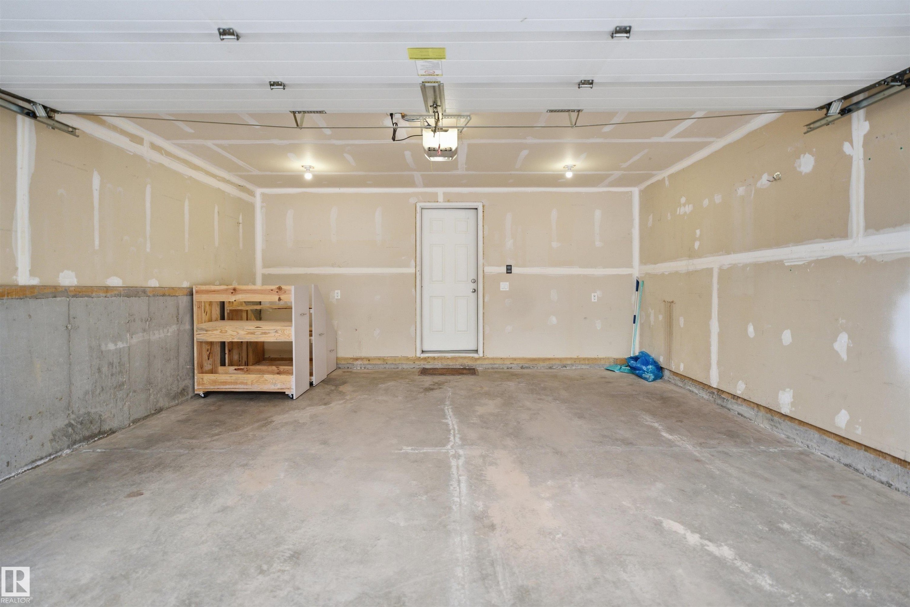 Spacious garage featuring a concrete floor, exposed drywall, overhead lighting fixtures, and a white access door - 33 7385 Edgemont Way Nw, Edmonton, AB - Indoor Photo Showing Garage