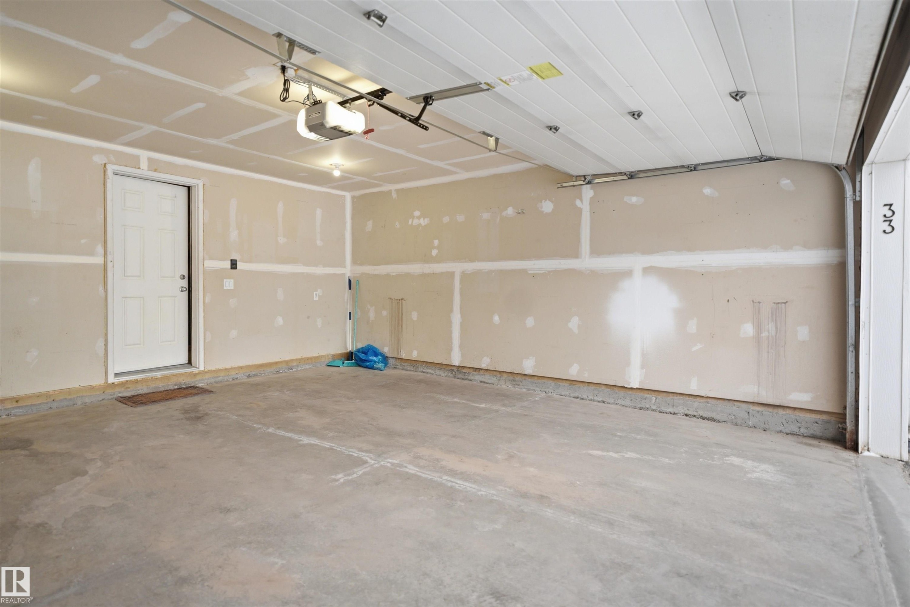 Spacious two-car garage featuring a concrete floor, an overhead garage door, interior access door, and an automatic garage door opener - 33 7385 Edgemont Way Nw, Edmonton, AB - Indoor Photo Showing Garage