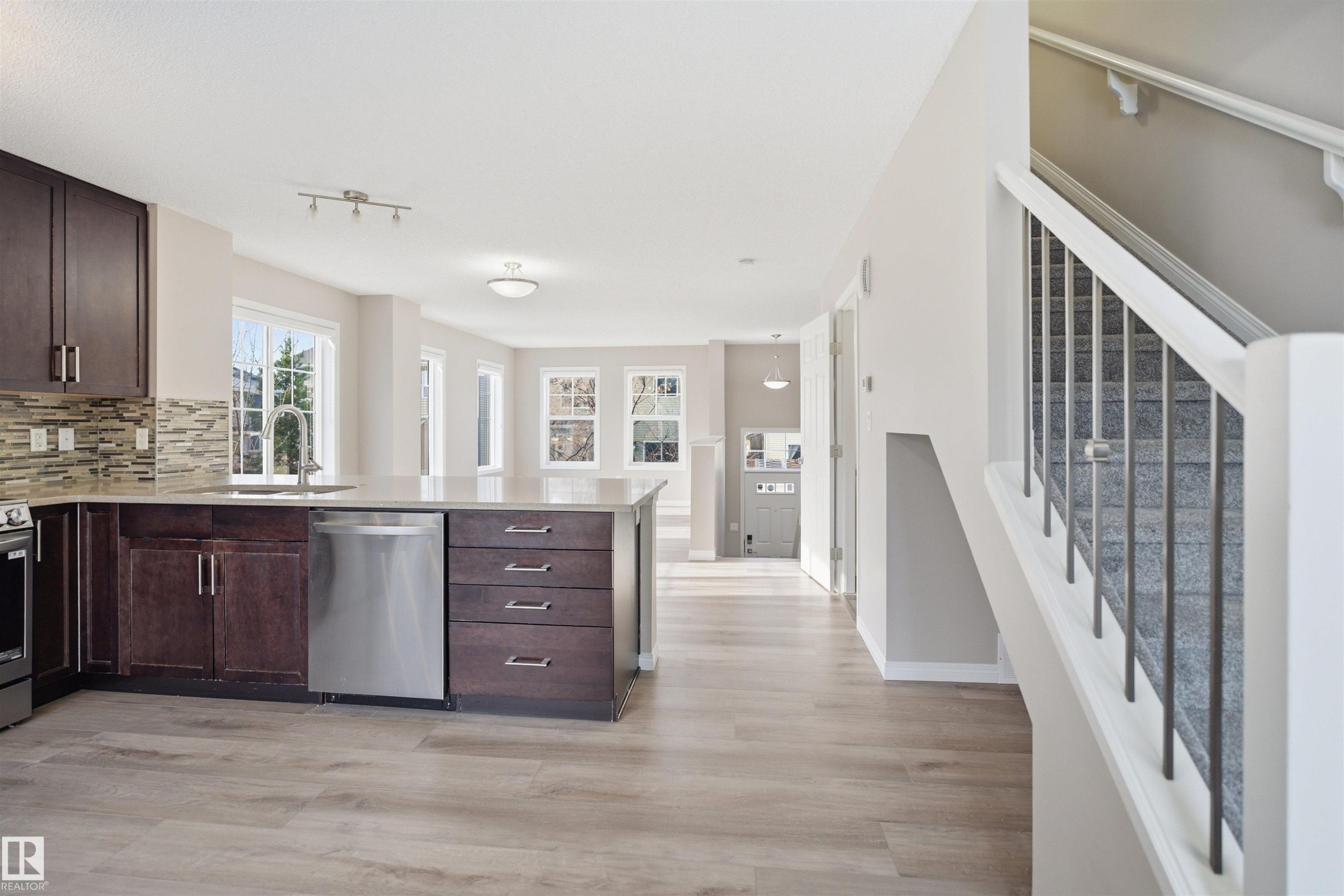Open-concept kitchen featuring dark wood cabinetry, light-toned countertops, stainless steel appliances, and a tiled backsplash - 33 7385 Edgemont Way Nw, Edmonton, AB - Indoor Photo Showing Kitchen