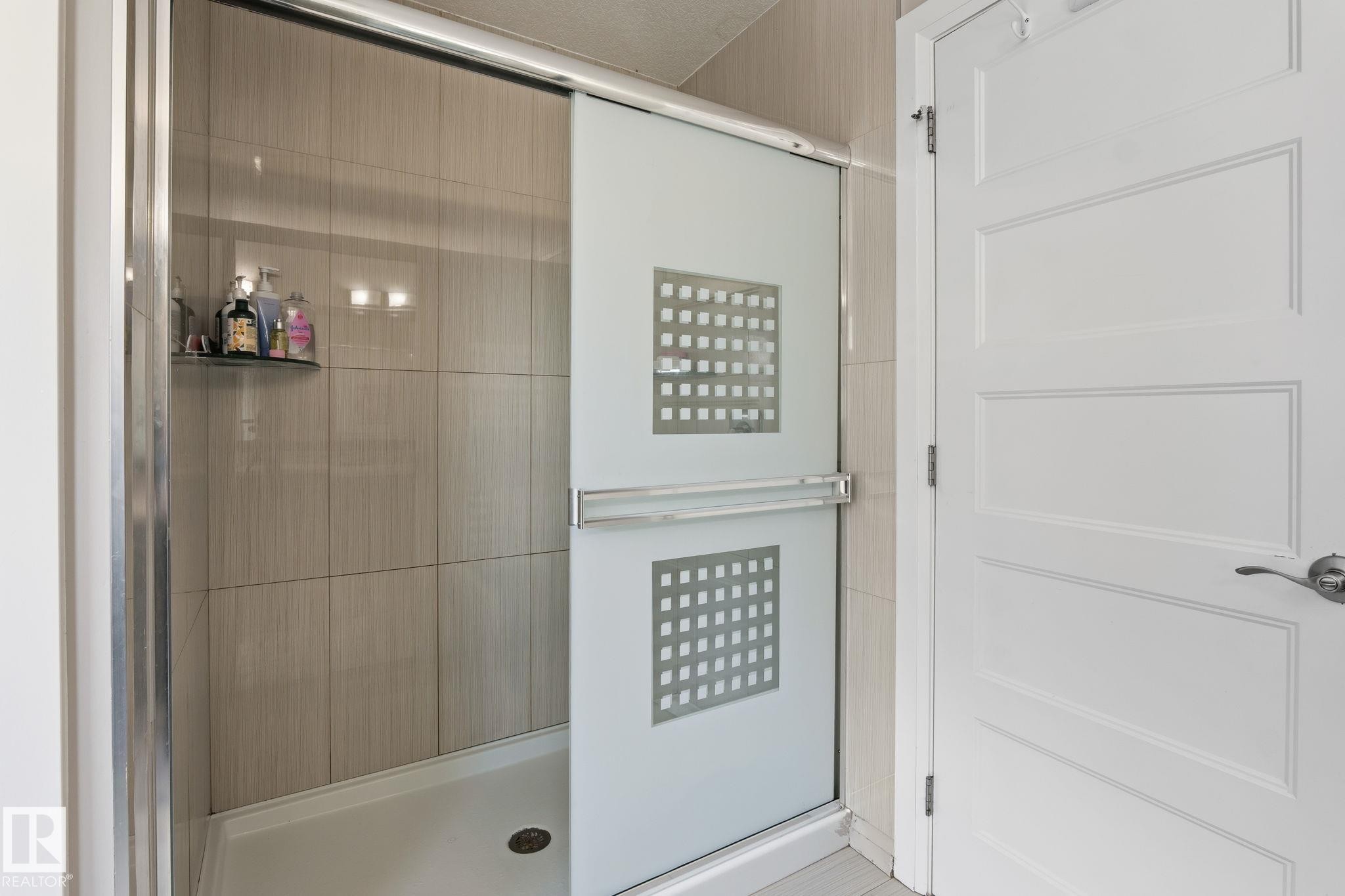 Tiled shower with sliding frosted glass enclosure and integrated shelf - 731 57 Street Sw, Edmonton, AB - Indoor Photo Showing Bathroom