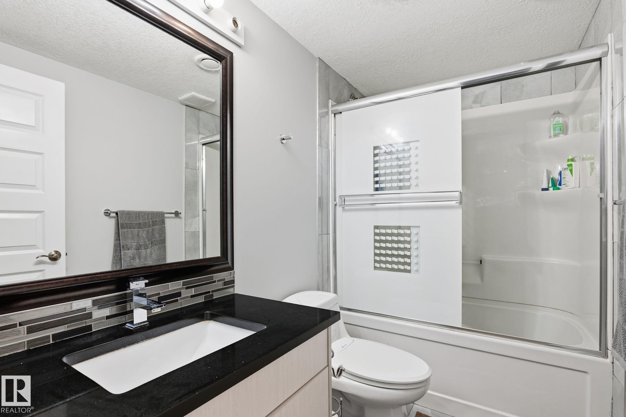 Bathroom featuring a dark framed mirror, vanity with an integrated sink, dark countertop, and a mosaic tile backsplash - 731 57 Street Sw, Edmonton, AB - Indoor Photo Showing Bathroom