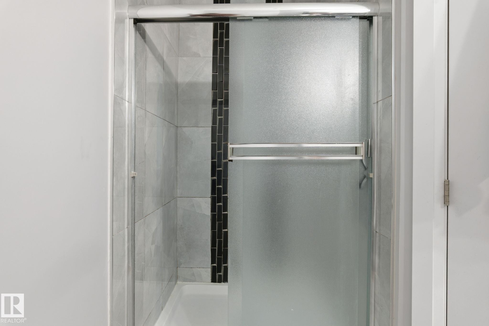 Shower enclosure with frosted glass sliding door, chrome hardware, light gray tile surround, and a vertical black mosaic tile accent strip - 731 57 Street Sw, Edmonton, AB - Indoor Photo Showing Bathroom