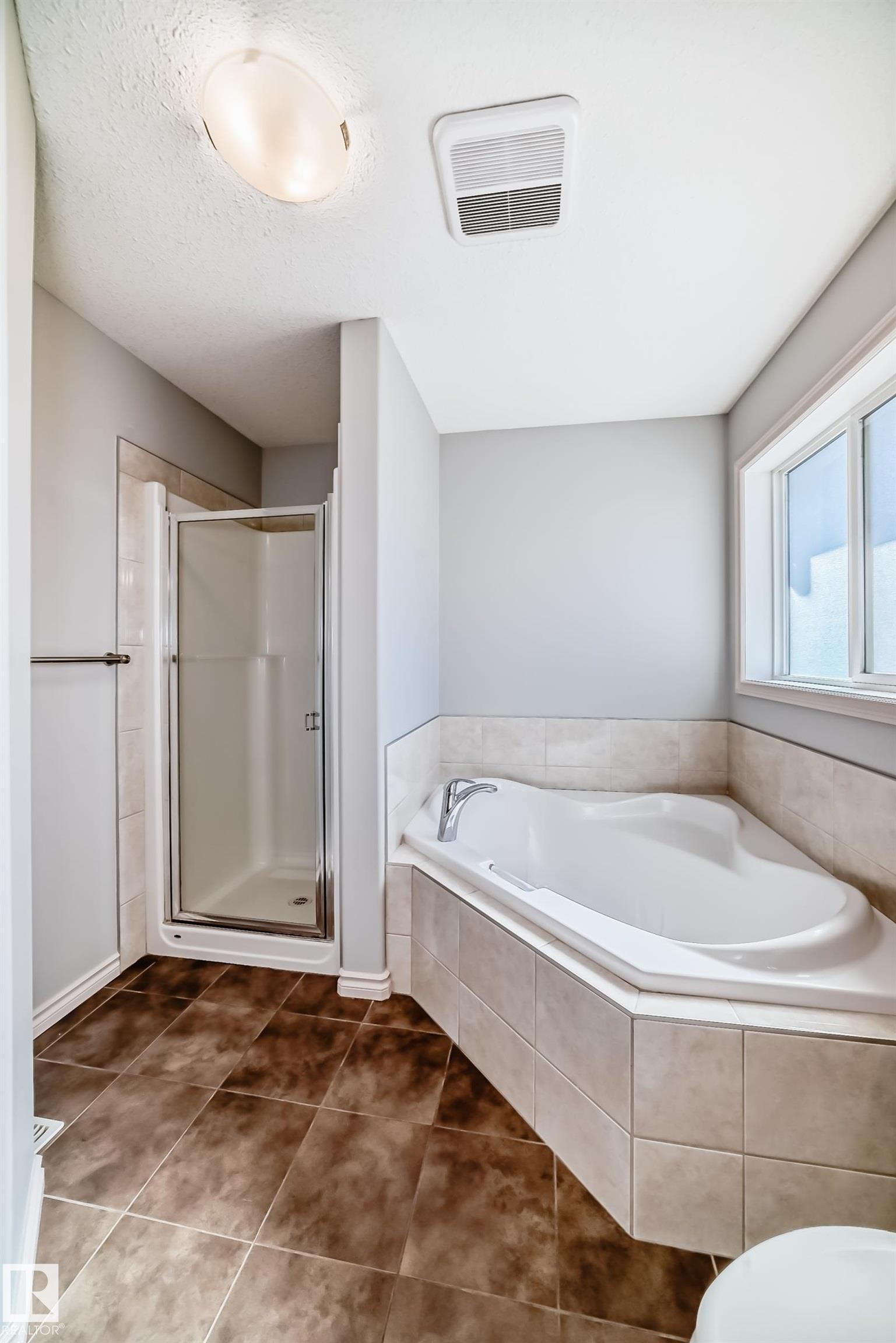 Corner soaking tub with tiled surround, walk-in shower with glass enclosure, brown tile flooring, and a large window - 6723 19 Avenue, Edmonton, AB - Indoor Photo Showing Bathroom