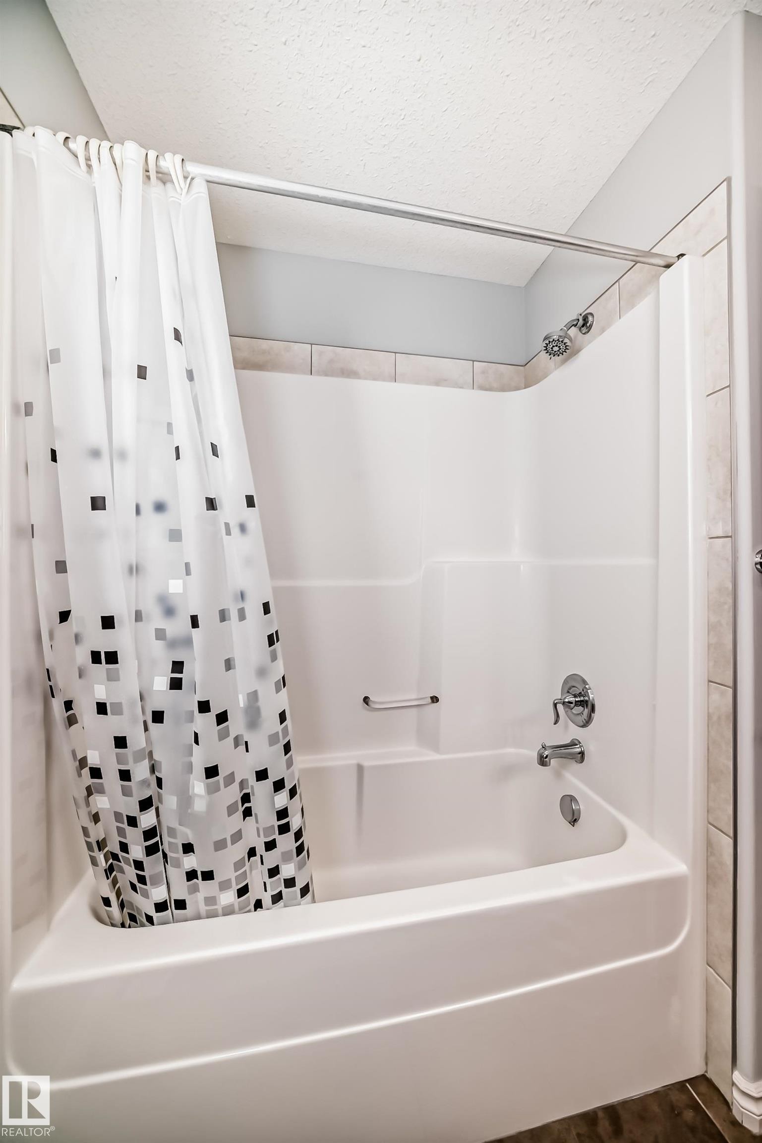 Bathtub and shower combination featuring a white composite surround, chrome fixtures, and a tile accent border - 6723 19 Avenue, Edmonton, AB - Indoor Photo Showing Bathroom