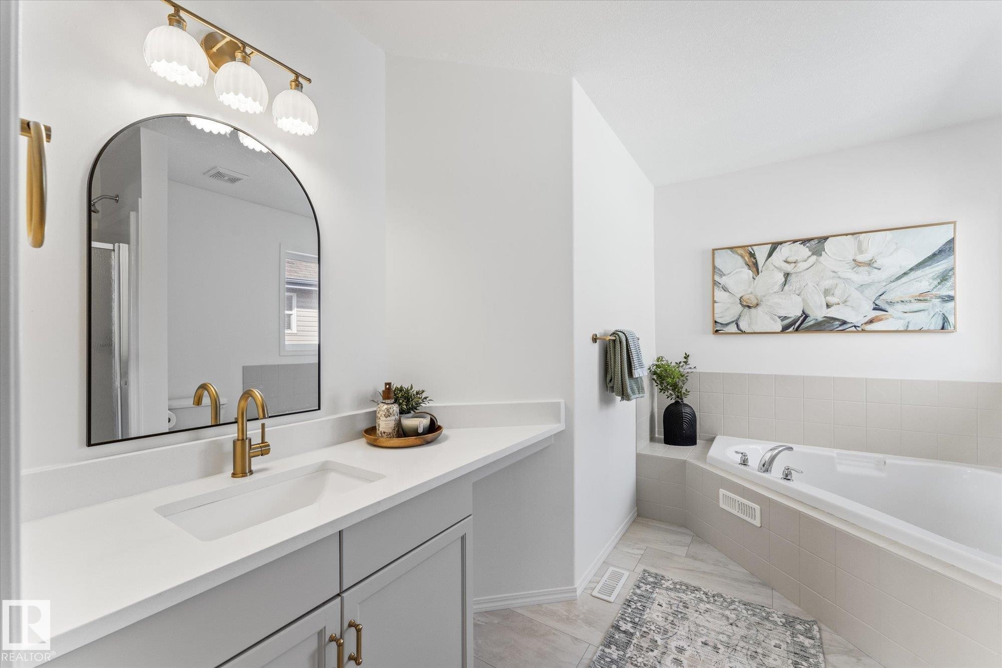 Contemporary bathroom featuring a spacious white countertop with an integrated sink, light-colored cabinetry with brass hardware, and a large arched mirror - 326 Silver Berry Road, Edmonton, AB - Indoor Photo Showing Bathroom
