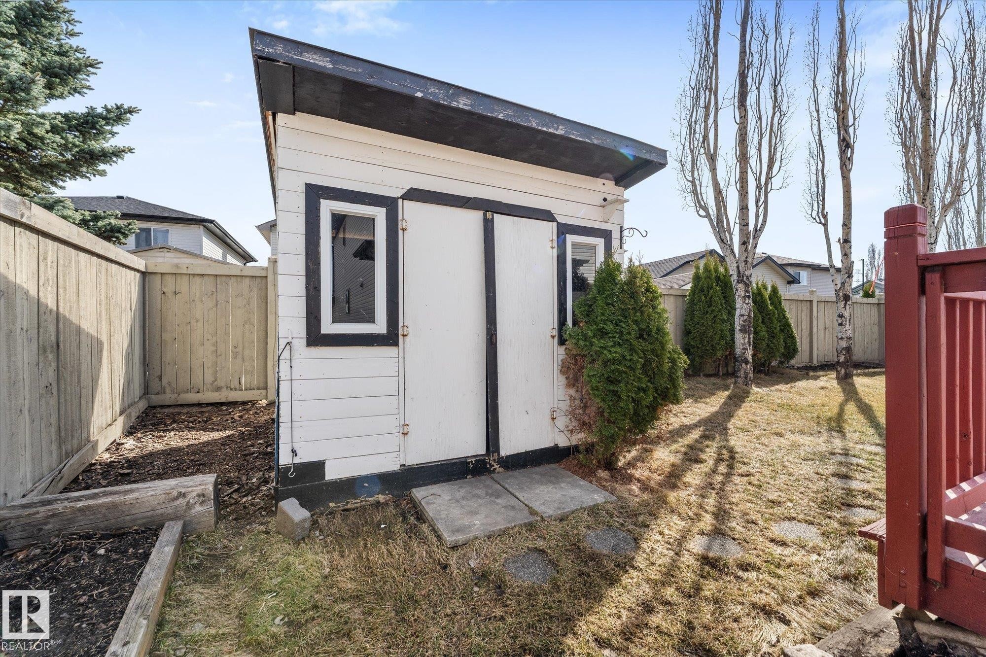 Freestanding storage shed with white siding and black trim, featuring dual entry doors and a single window - 326 Silver Berry Road, Edmonton, AB - Outdoor