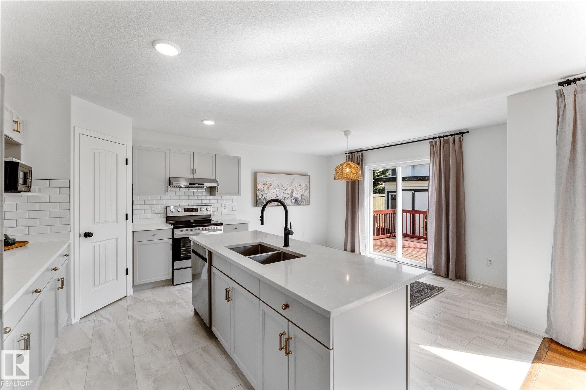 Kitchen featuring a large central island with an undermount sink, light-toned cabinetry with gold-toned hardware, white subway tile backsplash, and stainless steel appliances - 326 Silver Berry Road, Edmonton, AB - Indoor Photo Showing Kitchen With Double Sink With Upgraded Kitchen