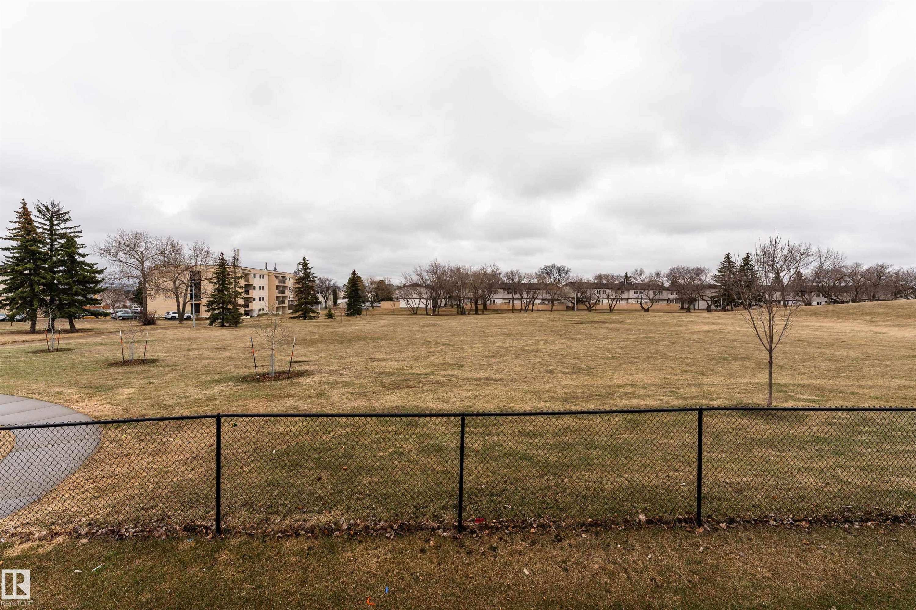 Expansive green space featuring a chain-link fence, mature trees, and a paved pathway - 15 5203 149 Avenue, Edmonton, AB - Outdoor With View