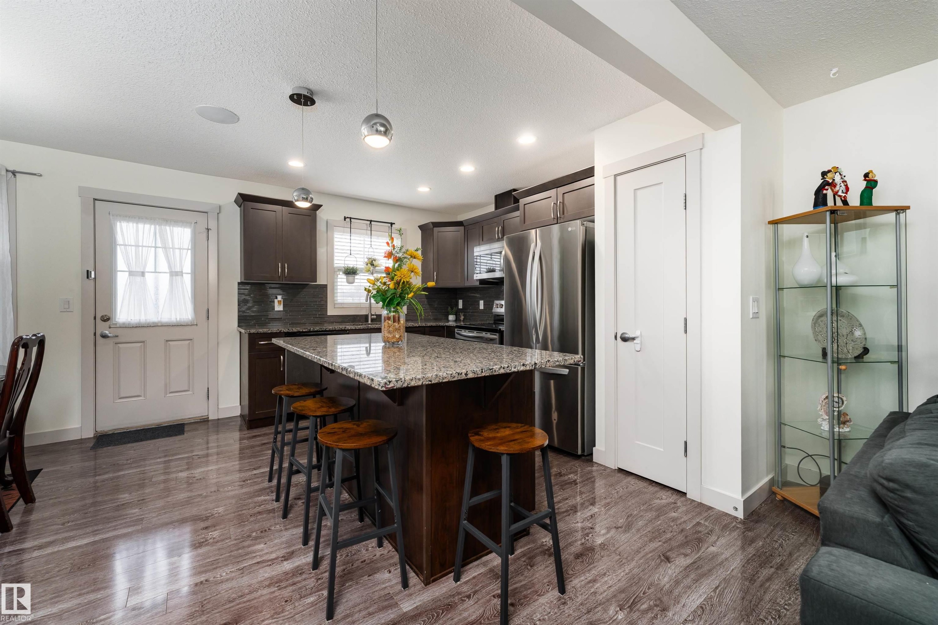 Kitchen featuring a central island with granite countertop, dark wood-finish cabinetry, stainless steel appliances, and wood-finish flooring - 15 5203 149 Avenue, Edmonton, AB - Indoor
