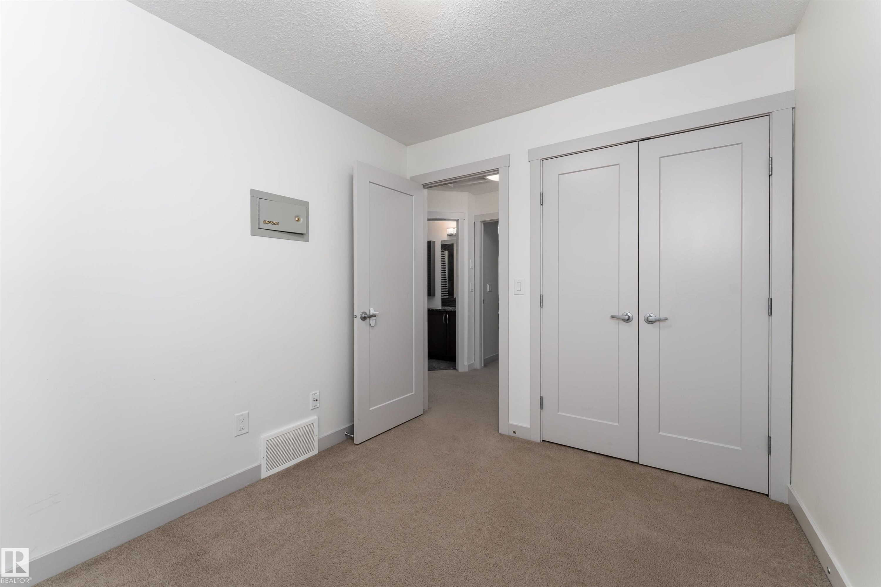 Neutral-toned carpeting extends throughout this interior space, featuring a double-door closet with brushed nickel hardware and a single interior door - 15 5203 149 Avenue, Edmonton, AB - Indoor Photo Showing Other Room
