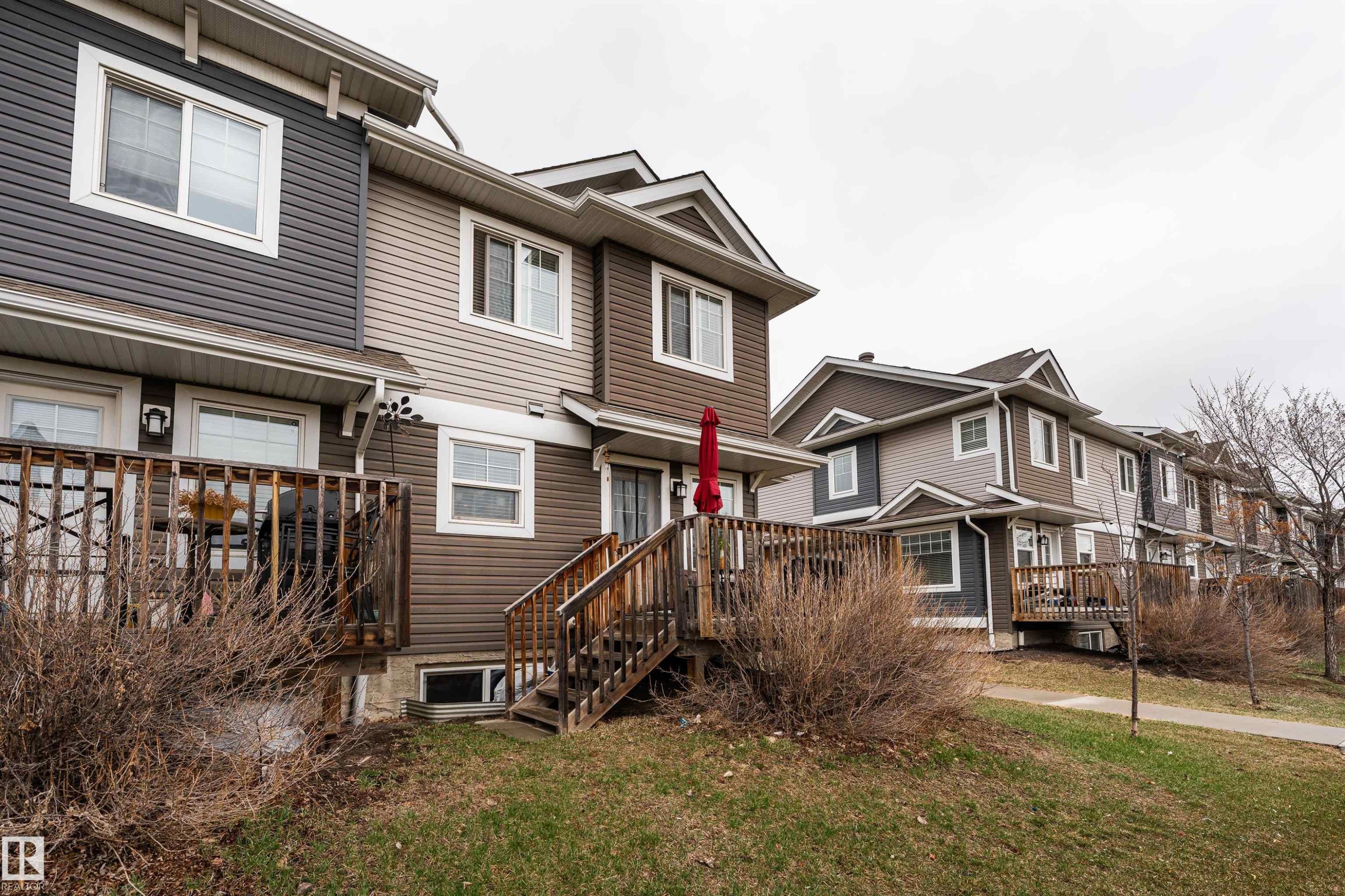 Townhouse exterior featuring multi-toned horizontal siding, white trim windows, and pitched shingle roofs - 15 5203 149 Avenue, Edmonton, AB - Outdoor With Deck Patio Veranda