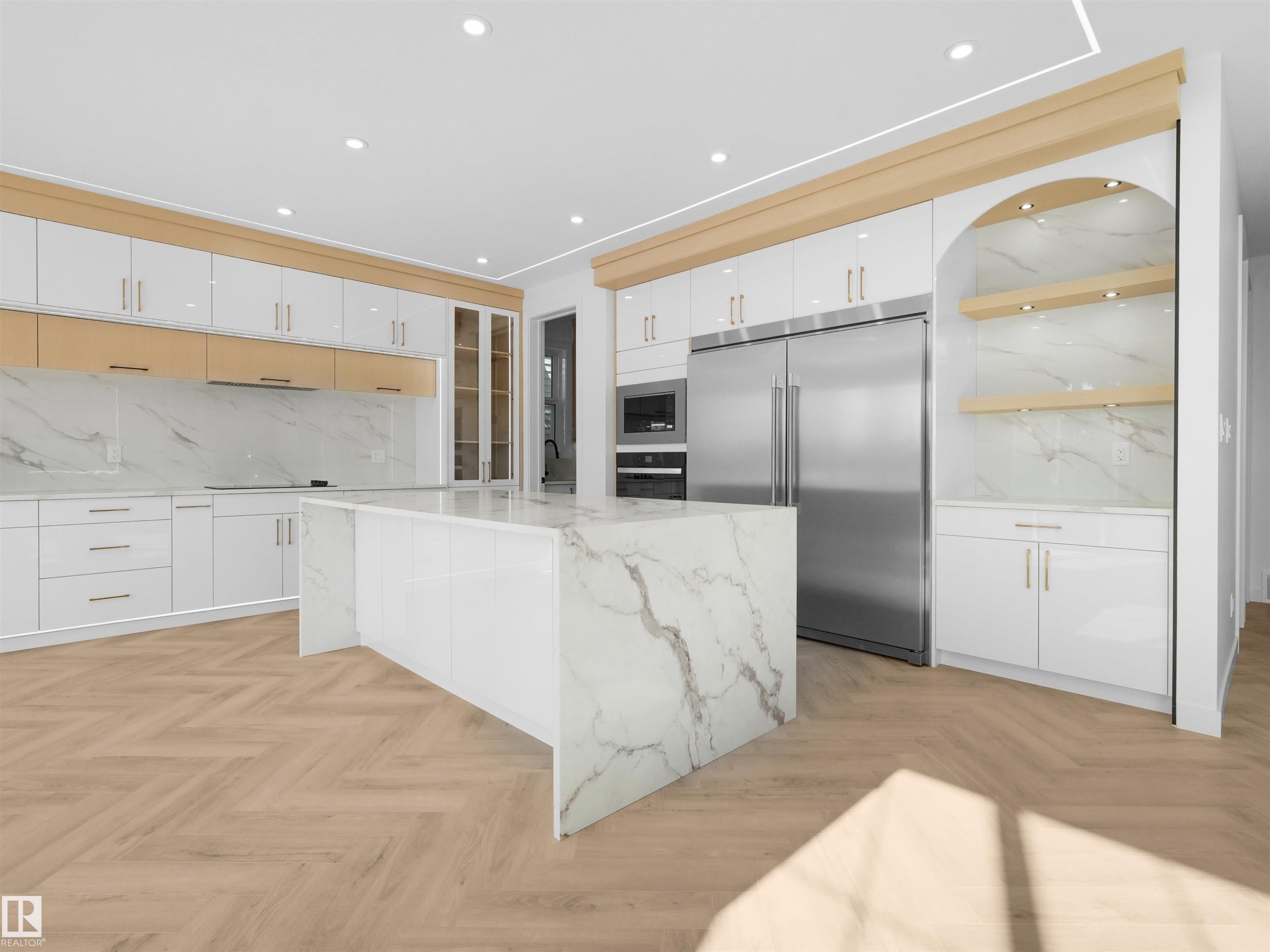 Spacious kitchen featuring a large waterfall-edge island, herringbone wood-finish flooring, integrated stainless steel appliances, white high-gloss cabinetry, and a marble-finish backsplash - 2070 Collip Crescent Sw, Edmonton, AB - Indoor Photo Showing Kitchen With Upgraded Kitchen