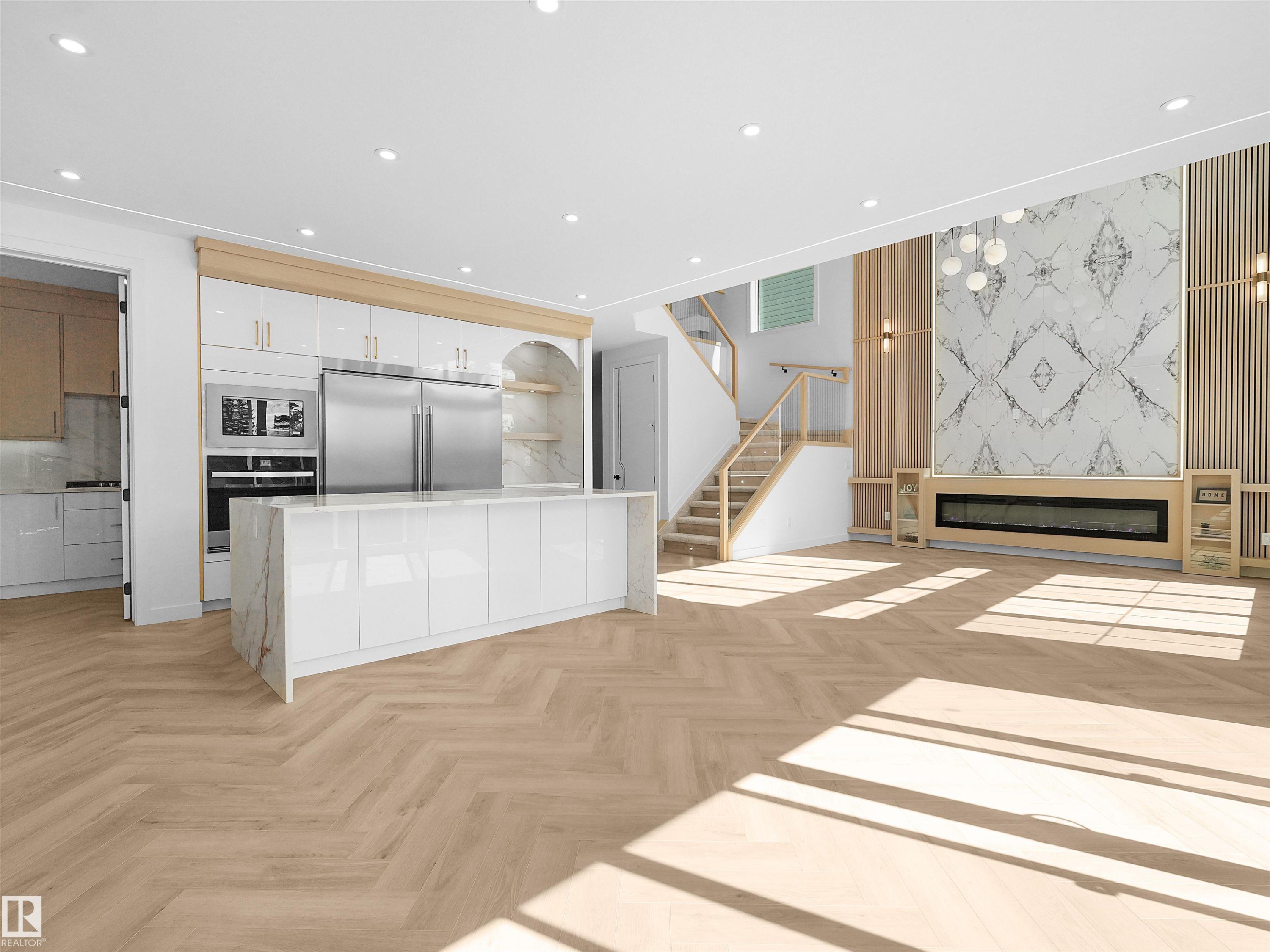 Open-concept interior featuring herringbone wood-finish flooring, a contemporary fireplace with a marble-patterned surround, and a kitchen island with a waterfall countertop - 2070 Collip Crescent Sw, Edmonton, AB - Indoor Photo Showing Kitchen With Upgraded Kitchen