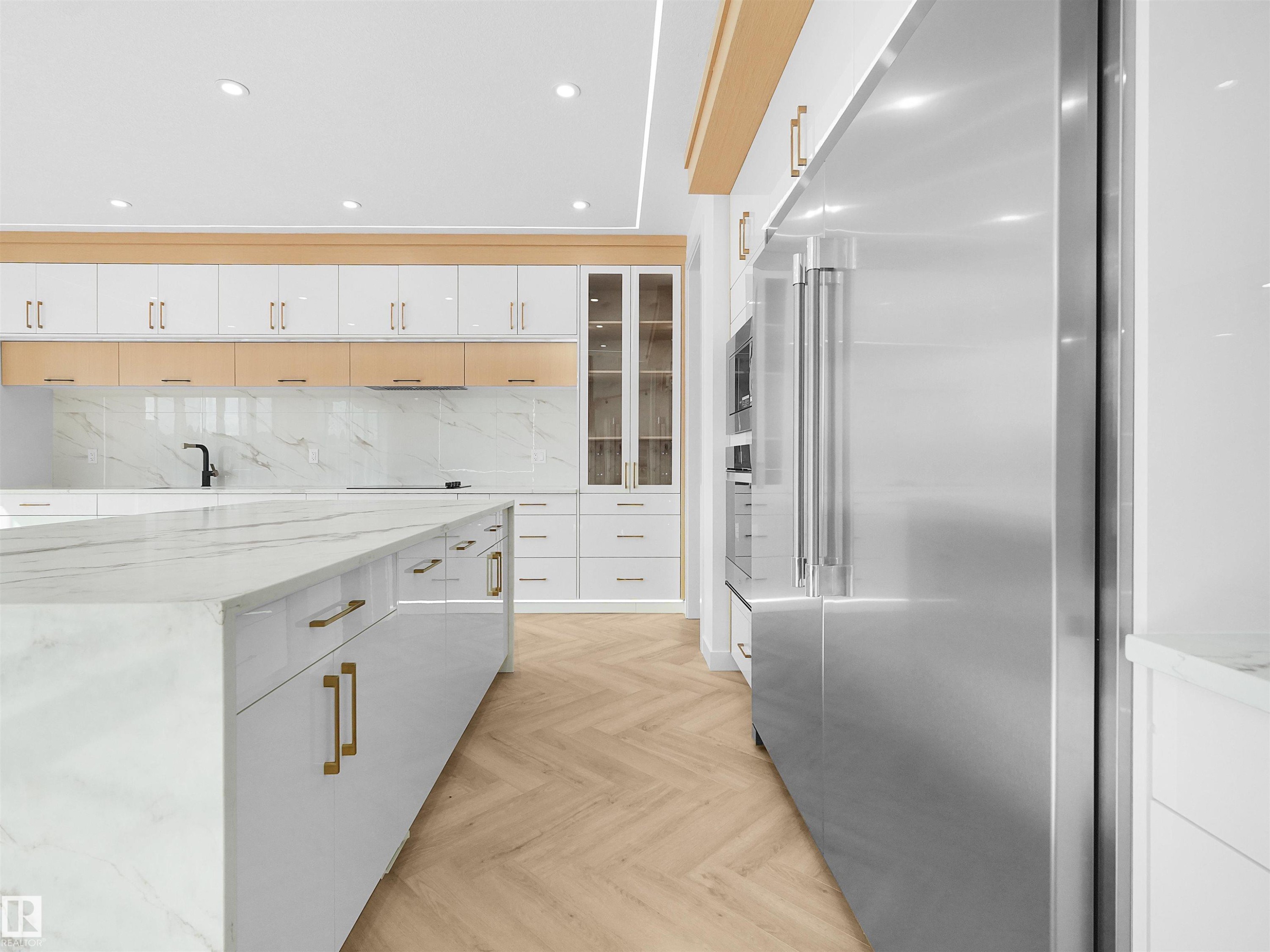 Gourmet kitchen featuring a large waterfall island with integrated storage, full-height backsplash, stainless steel appliances, and herringbone wood-finish flooring - 2070 Collip Crescent Sw, Edmonton, AB - Indoor Photo Showing Kitchen