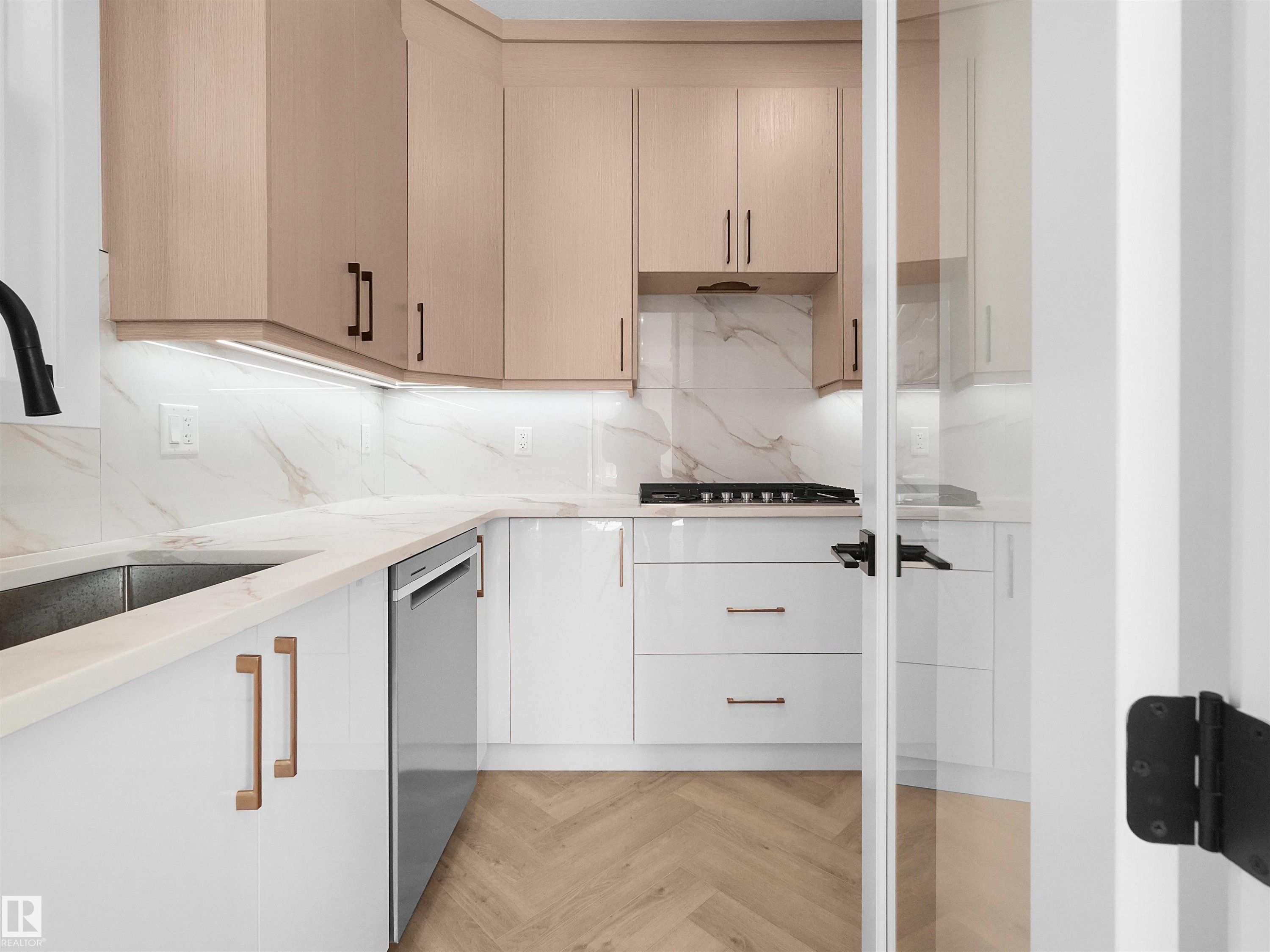 Butlers Kitchen featuring two-tone cabinetry with under-cabinet lighting, a built-in gas range, a stainless steel dishwasher, and a herringbone-pattern wood-finish floor - 2070 Collip Crescent Sw, Edmonton, AB - Indoor Photo Showing Kitchen