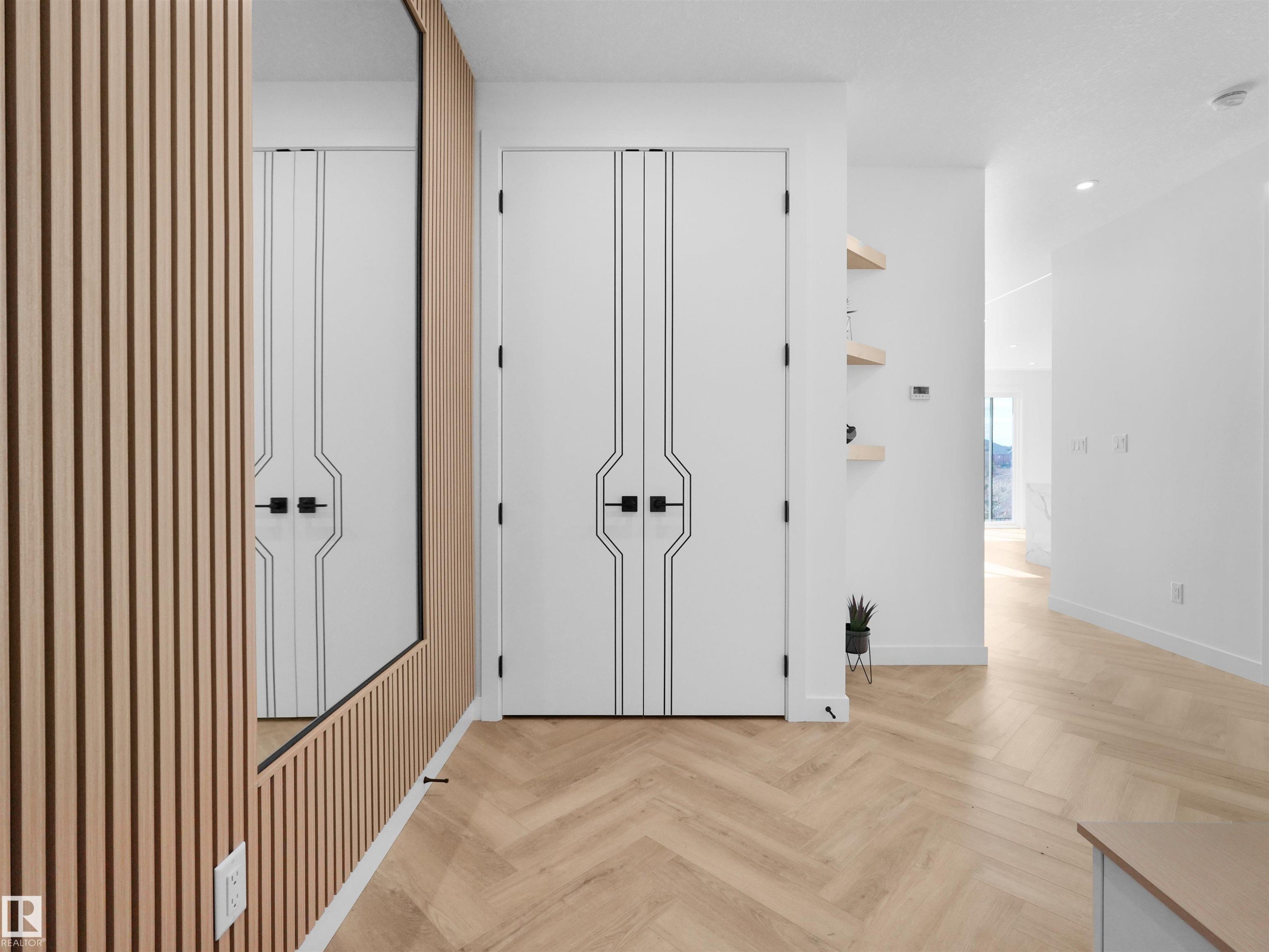 Entryway featuring light wood-finish herringbone flooring, a full-length mirror with slatted wood-finish paneling, and modern white doors with geometric detailing and black hardware - 2070 Collip Crescent Sw, Edmonton, AB - Indoor Photo Showing Other Room