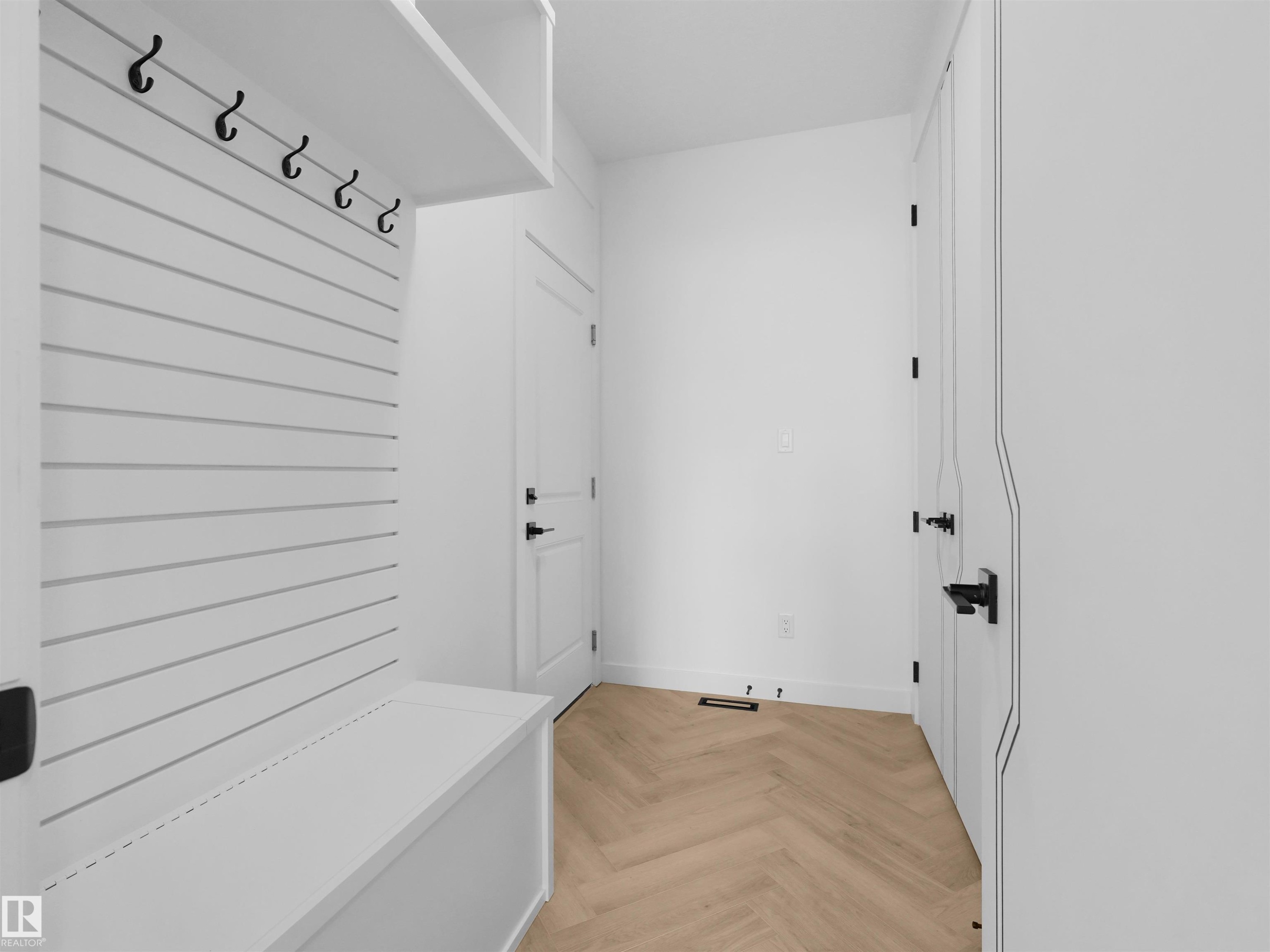 Entryway mudroom featuring herringbone wood-finish flooring, built-in white bench, shiplap-style wall paneling with hooks, overhead shelving, and multiple white doors with matte black hardware - 2070 Collip Crescent Sw, Edmonton, AB - Indoor Photo Showing Other Room