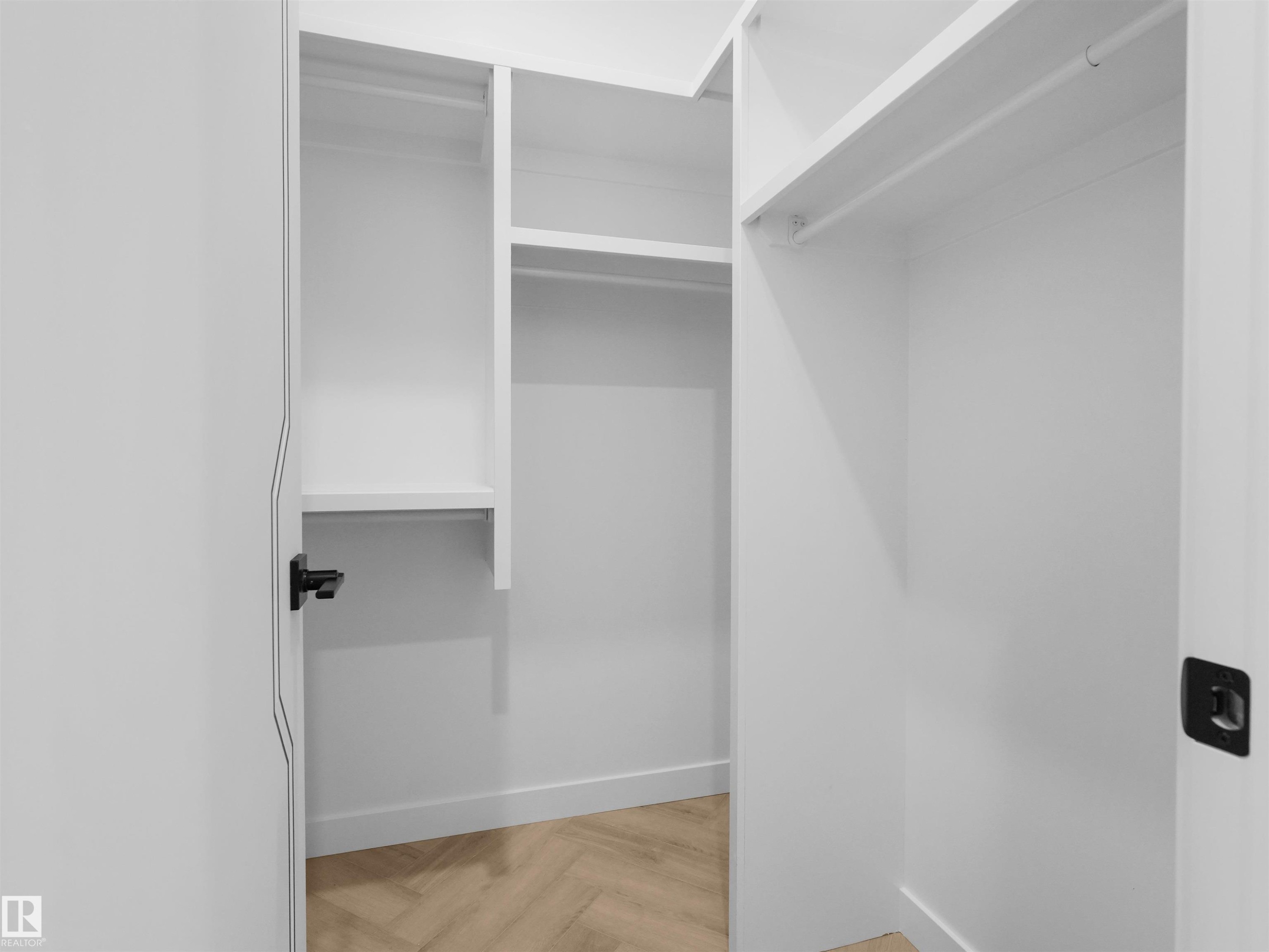 Walk-in closet featuring white built-in shelving, hanging rods, and wood-finish flooring in a herringbone pattern - 2070 Collip Crescent Sw, Edmonton, AB - Indoor With Storage