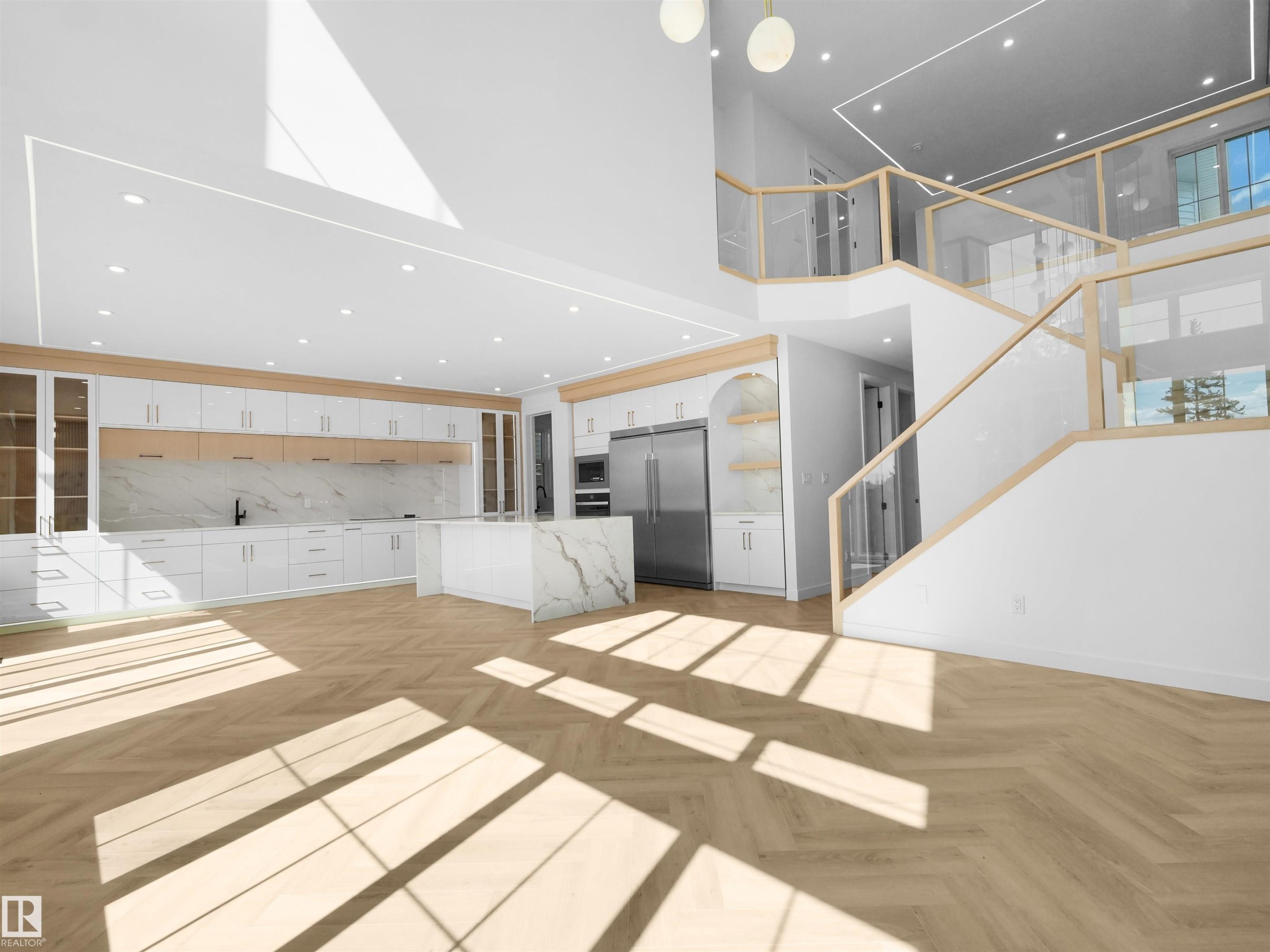 Open-concept interior featuring wood-finish herringbone flooring, a multi-level staircase with glass railings, a chef's kitchen with a waterfall island, and integrated stainless steel appliances - 2070 Collip Crescent Sw, Edmonton, AB - Indoor Photo Showing Other Room
