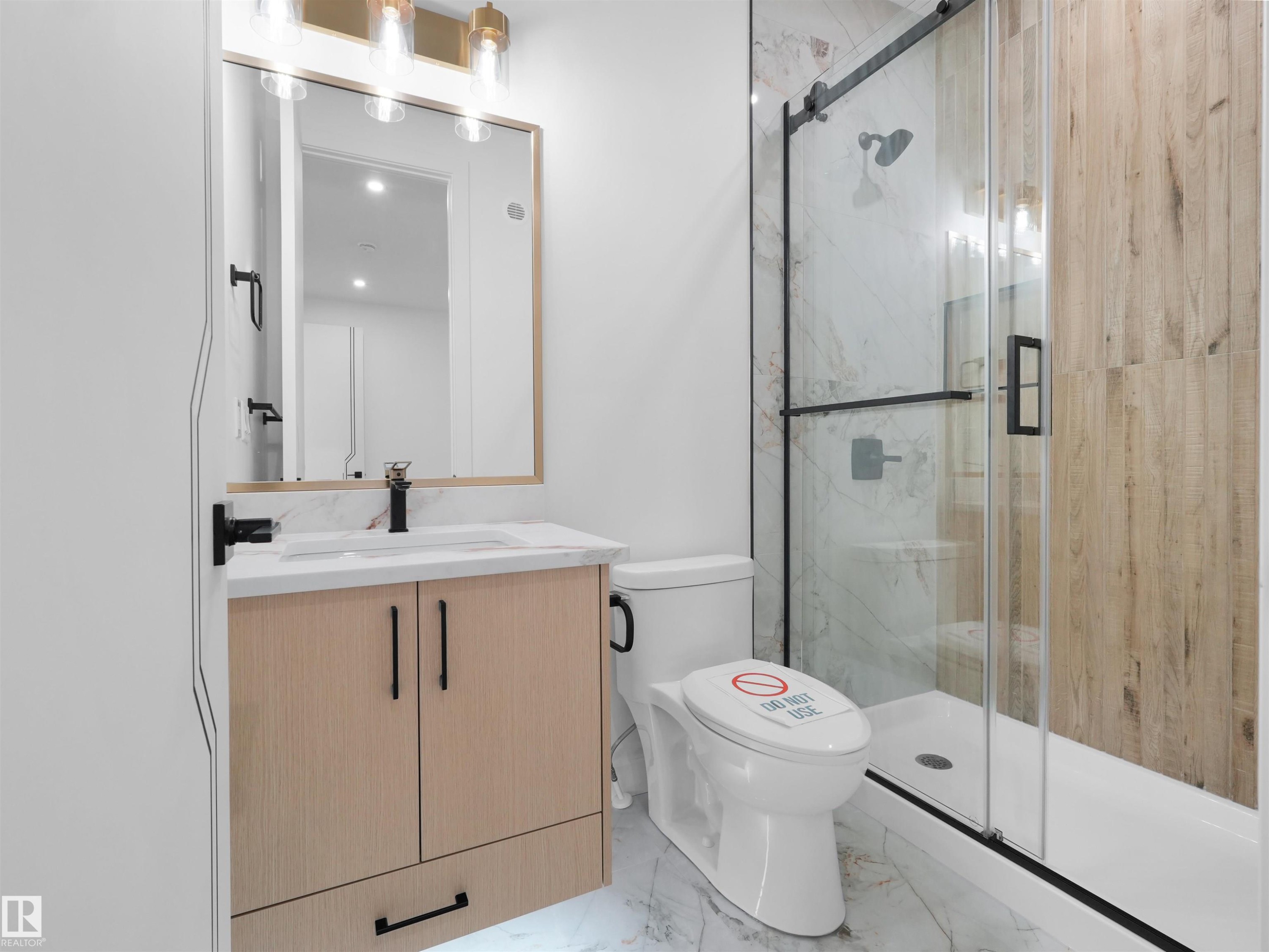 Modern bathroom featuring a single vanity with wood-finish cabinetry, a white countertop, and a black faucet - 2070 Collip Crescent Sw, Edmonton, AB - Indoor Photo Showing Bathroom