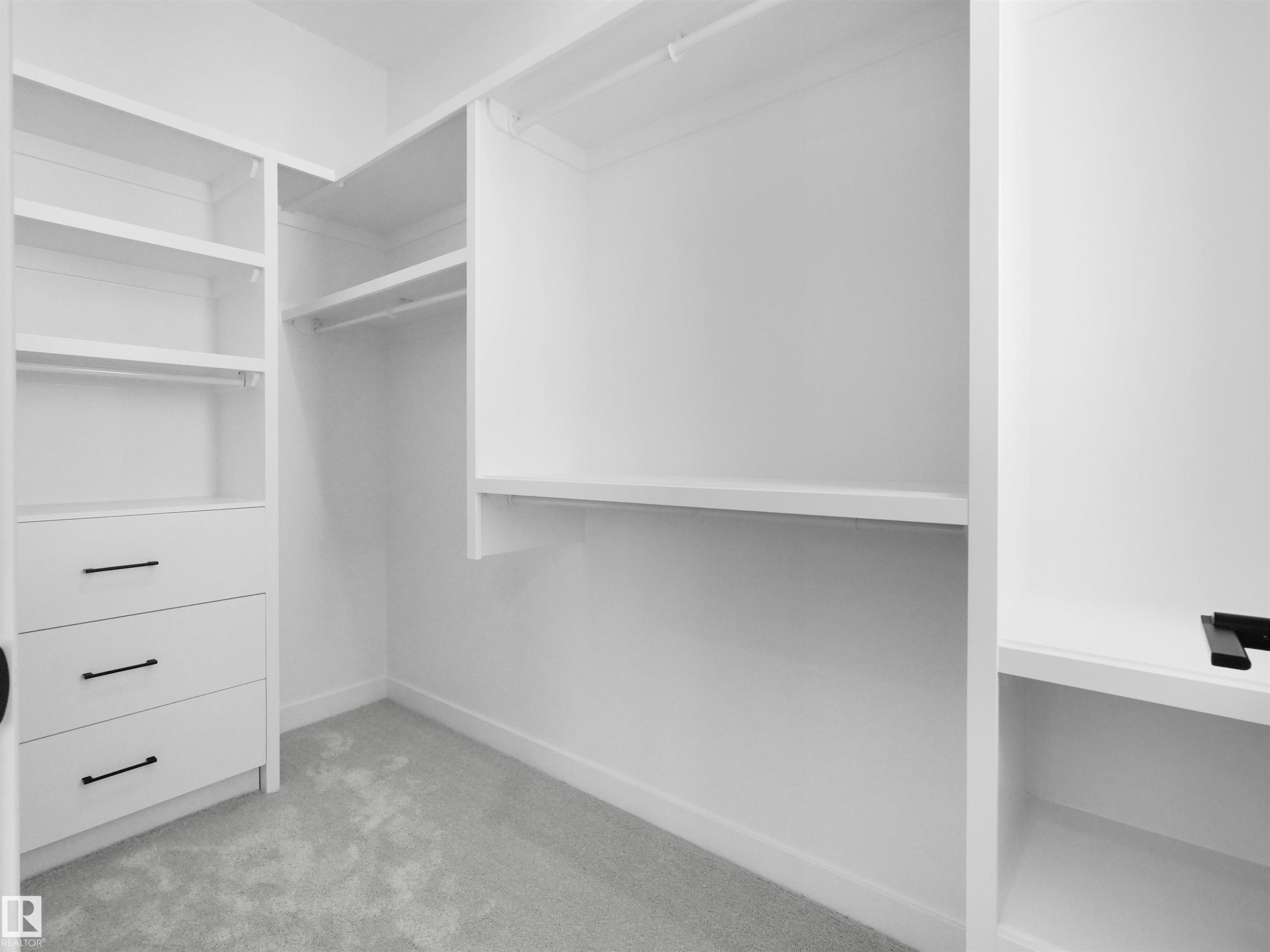 Walk-in closet featuring white built-in shelving, multiple hanging rods, three integrated drawers with black hardware, and light gray carpet - 2070 Collip Crescent Sw, Edmonton, AB - Indoor With Storage