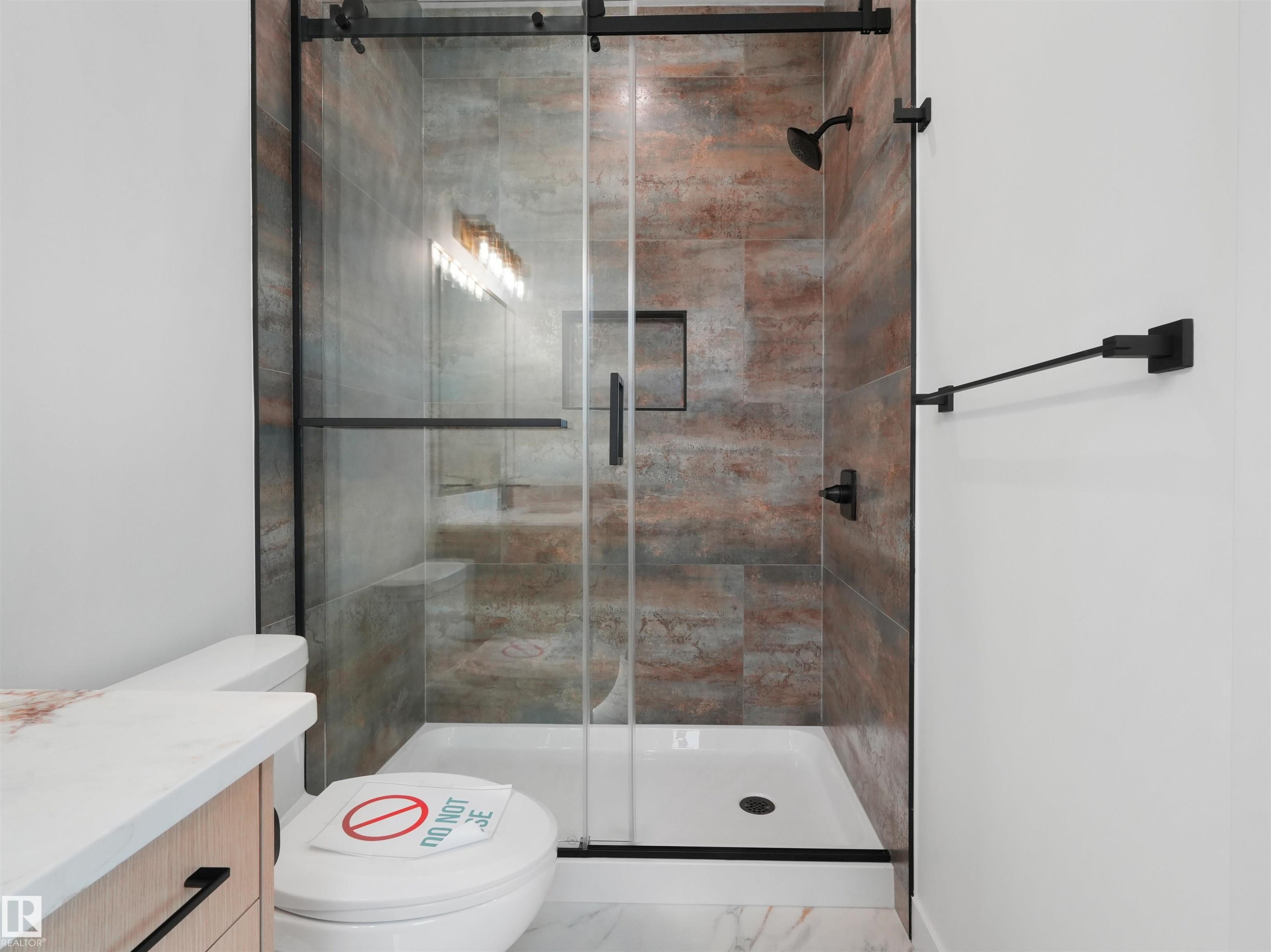 Frameless glass shower enclosure with matte black hardware, featuring rich multi-toned wall tiling and a built-in shower niche - 2070 Collip Crescent Sw, Edmonton, AB - Indoor Photo Showing Bathroom