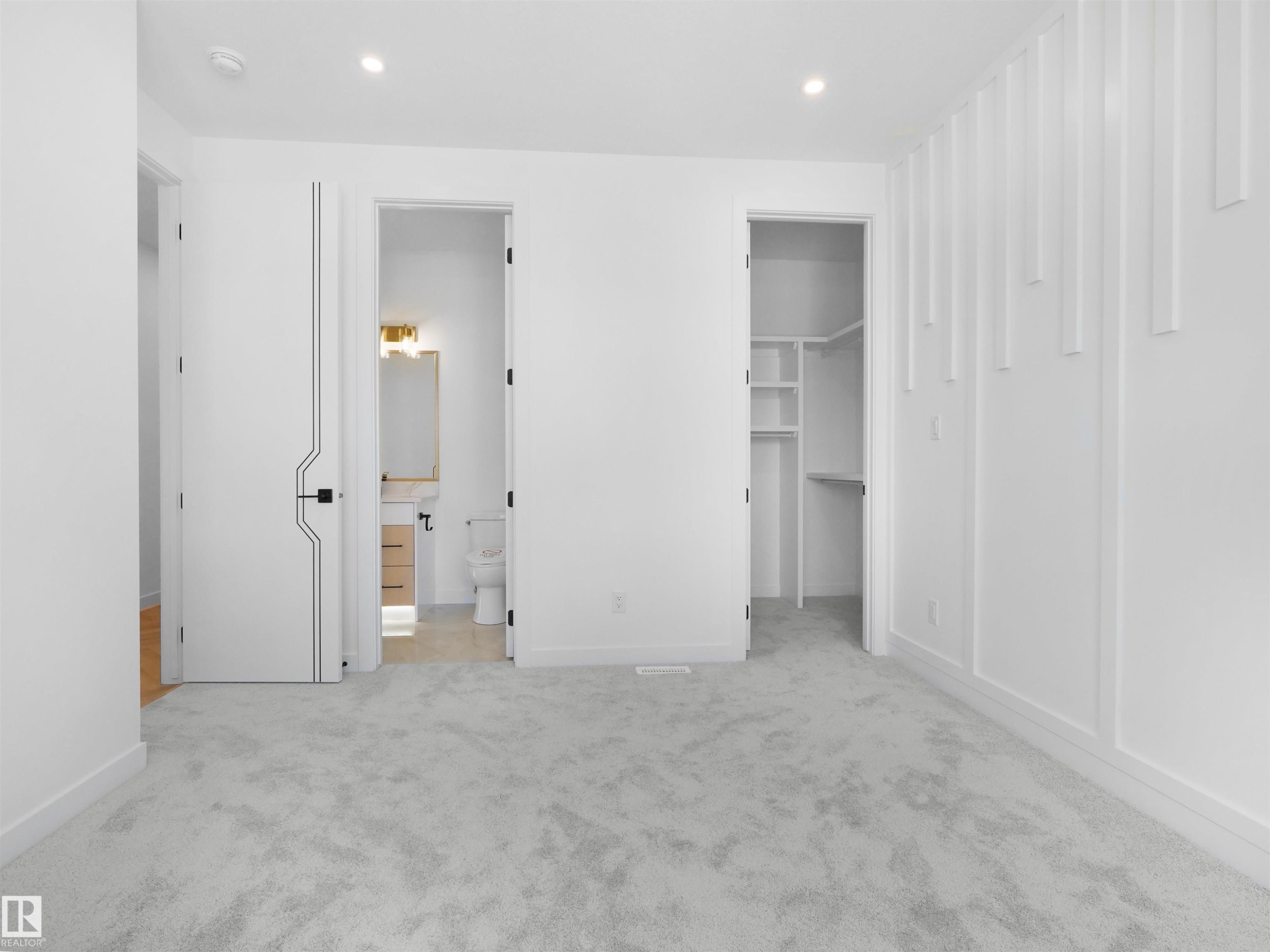 Carpeted interior space featuring a textured accent wall, built-in closet shelving, and a nearby bathroom with a vanity and toilet - 2070 Collip Crescent Sw, Edmonton, AB - Indoor Photo Showing Other Room