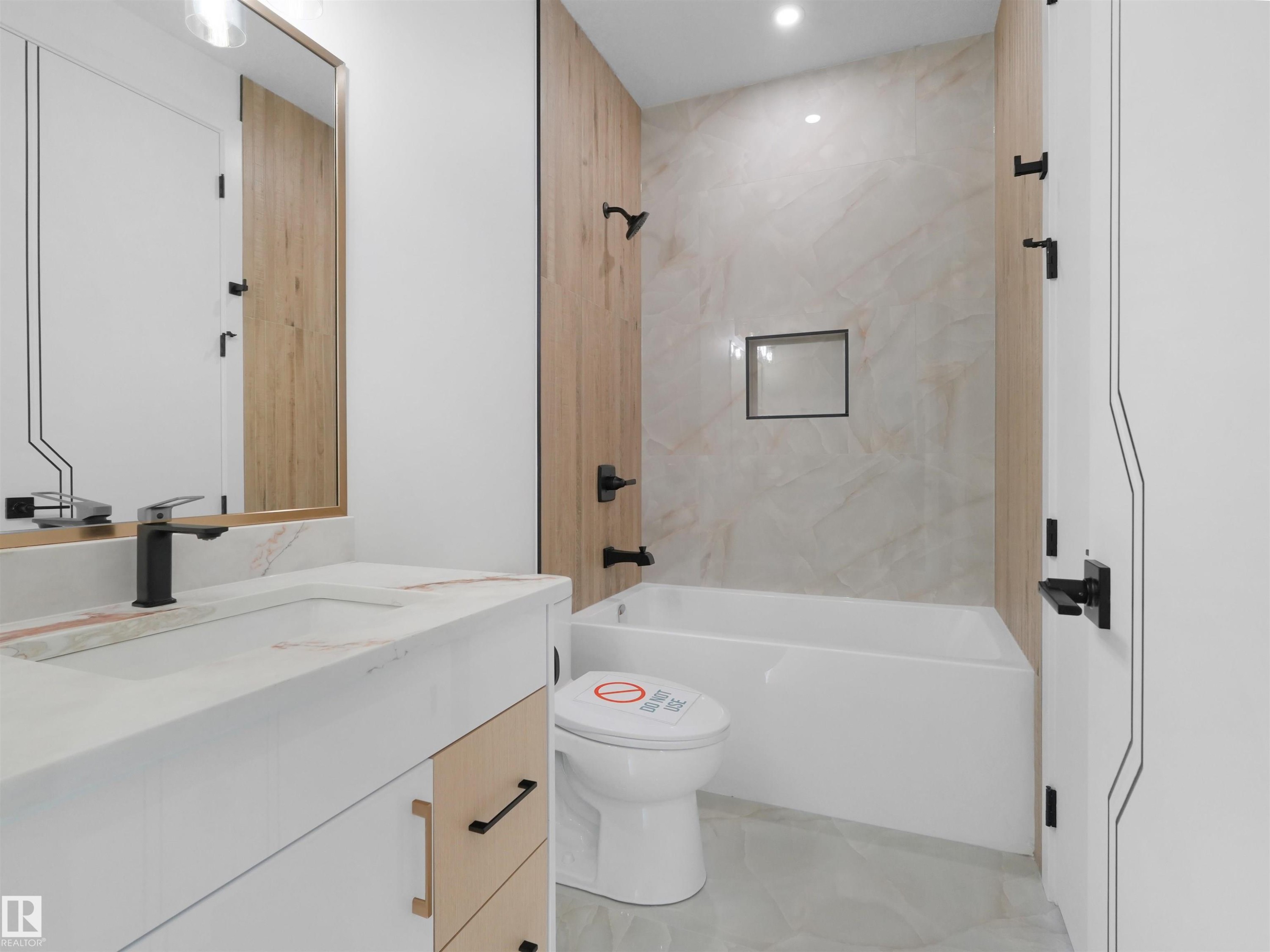 Modern bathroom featuring a single vanity with a white countertop and integrated sink, matte black faucet, and wood-finish cabinetry - 2070 Collip Crescent Sw, Edmonton, AB - Indoor Photo Showing Bathroom