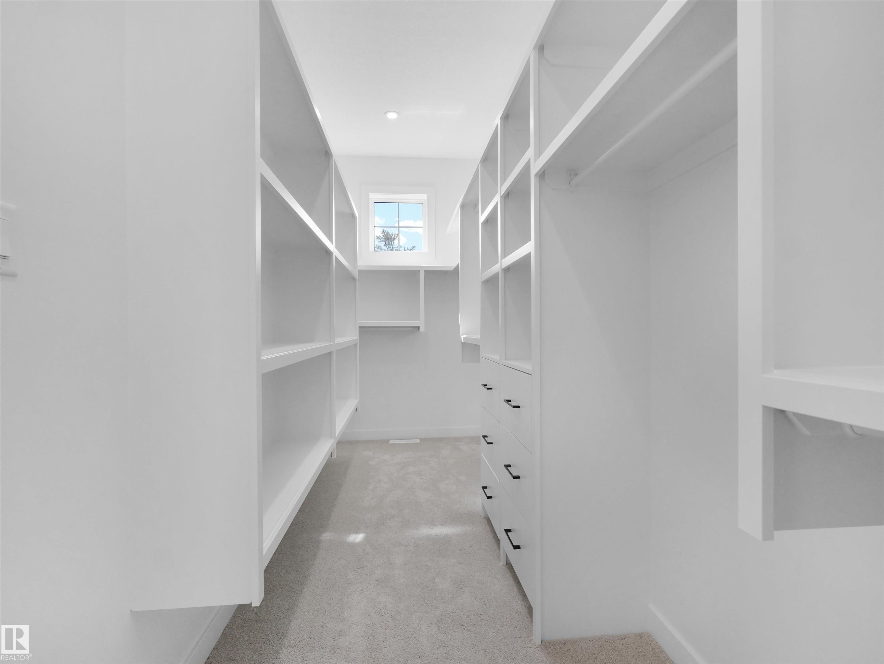 Walk-in closet featuring extensive built-in shelving, multiple hanging rods, integrated drawers with black pulls, recessed ceiling lighting, and a window providing natural illumination - 2070 Collip Crescent Sw, Edmonton, AB - Indoor With Storage