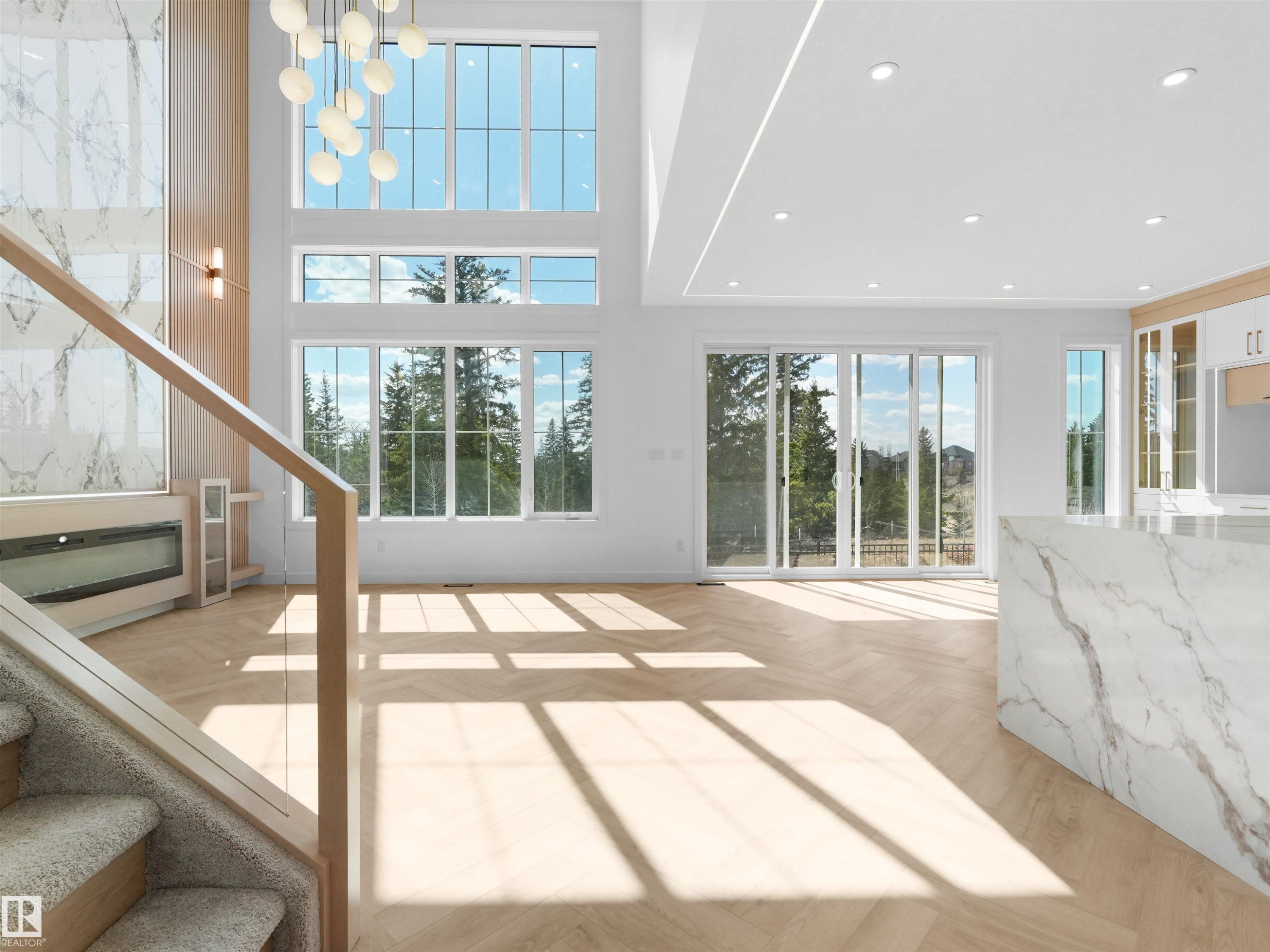 Two-story living area featuring extensive window treatments, modern chandelier, integrated fireplace with stone-finish surround, and wood-finish flooring - 2070 Collip Crescent Sw, Edmonton, AB - Indoor Photo Showing Other Room